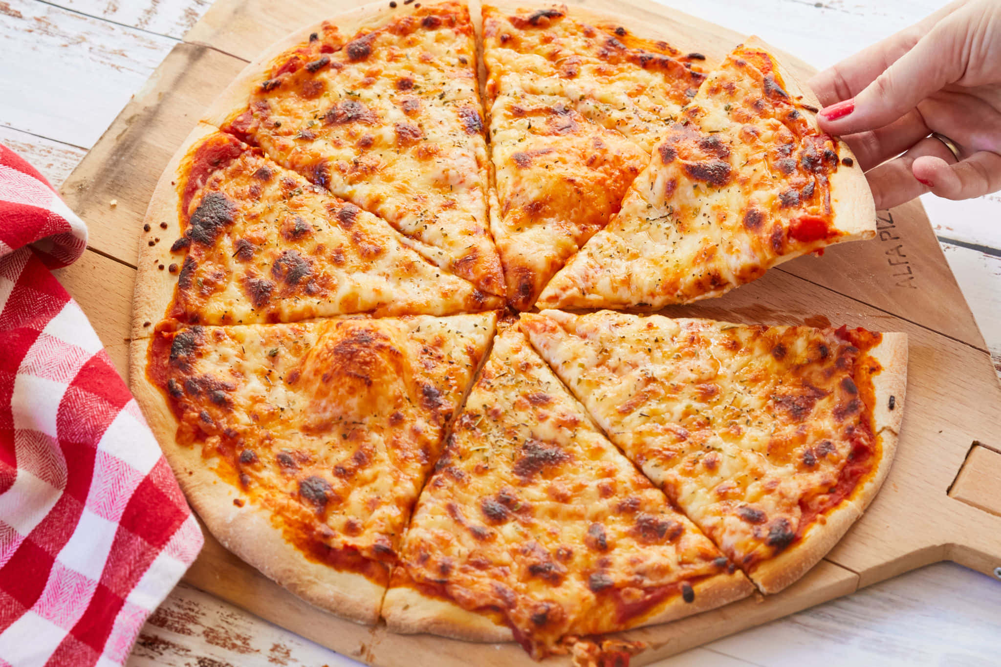 Pizza 桌布 壁紙 — 一隻手從木板上拿起一片起司瑪格麗特披薩，旁邊有一張紅色格子餐巾。