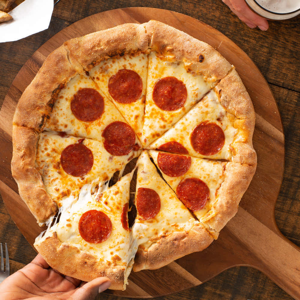 Pizza 桌布 壁紙 — 一隻手從木板上新鮮出爐的披薩上拿起一塊起司辣味香腸披薩片。