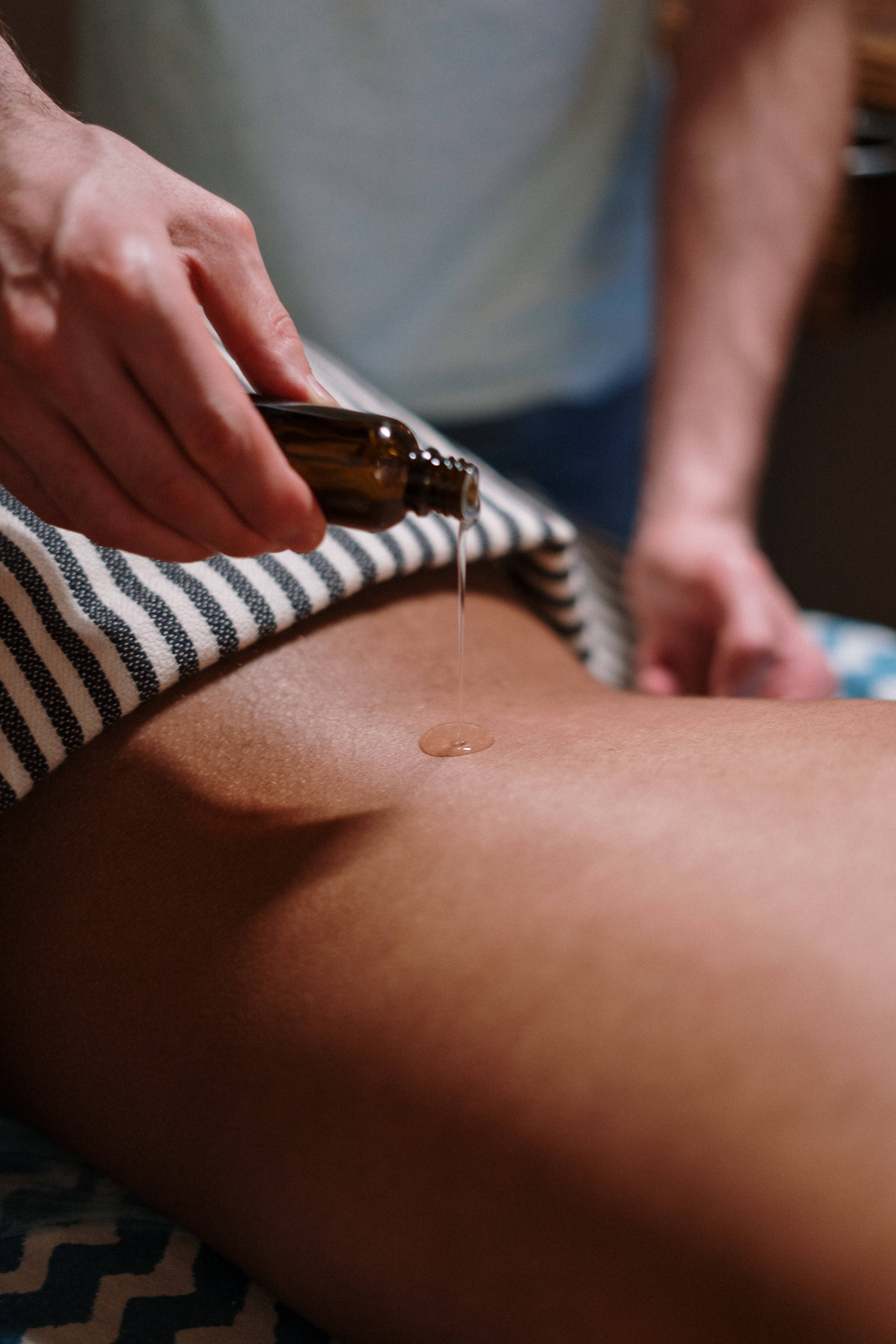 oil massage 桌布 壁紙 — 一隻手從深琥珀色瓶子將金色油倒在鋪著條紋毛巾的裸露大腿上。