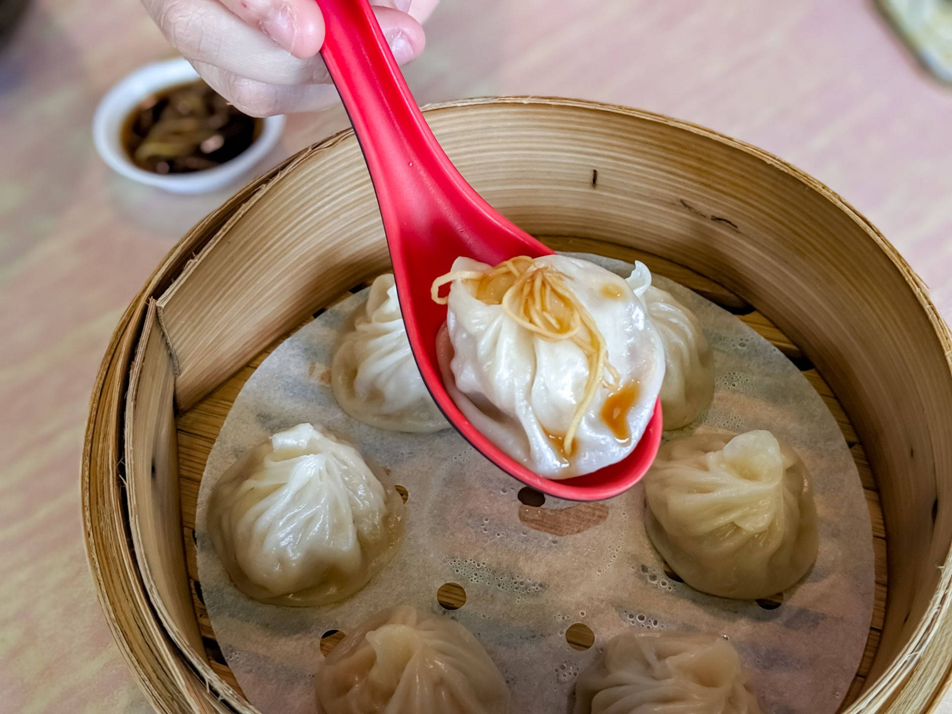 steam 桌布 壁紙 — 一隻手從裝滿更多餃子的竹蒸籠中拿起一個冒著熱氣的餃子，上面有薑絲和醬汁。
