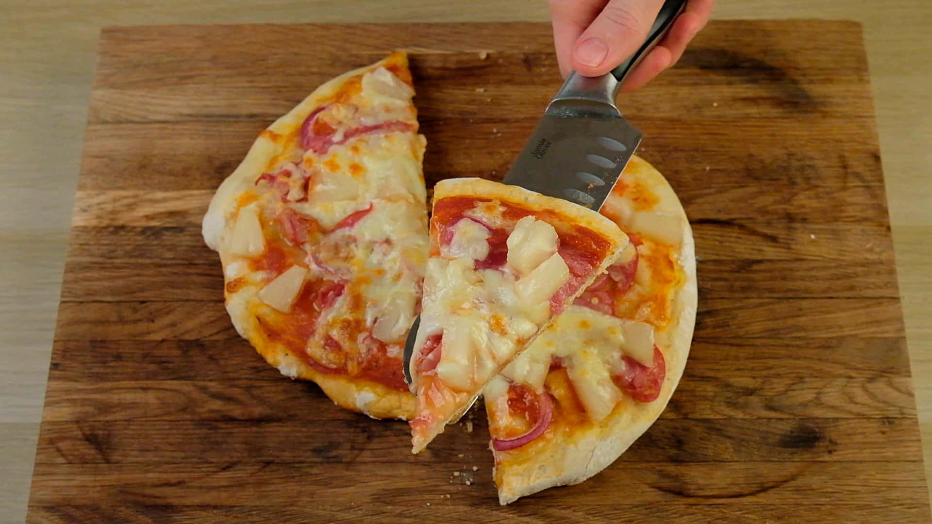 Pizza 桌布 壁紙 — 一隻手從質樸的木砧板上拿起一片夏威夷披薩，上面有鳳梨和火腿。