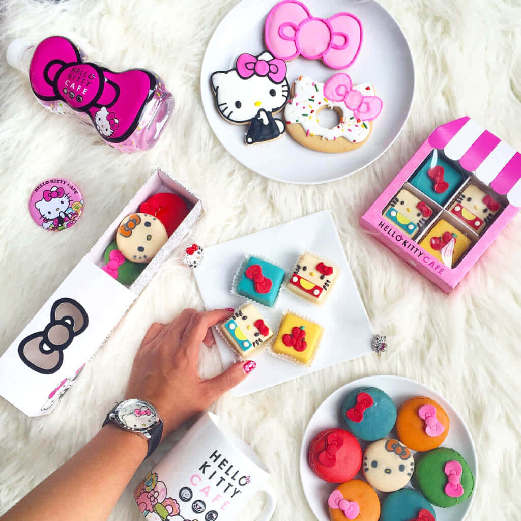 Hello Kitty 桌布 壁紙 — 一隻手從鋪在毛絨白色地毯上的色彩繽紛主題糕點和商品中拿起一塊Hello Kitty餅乾。