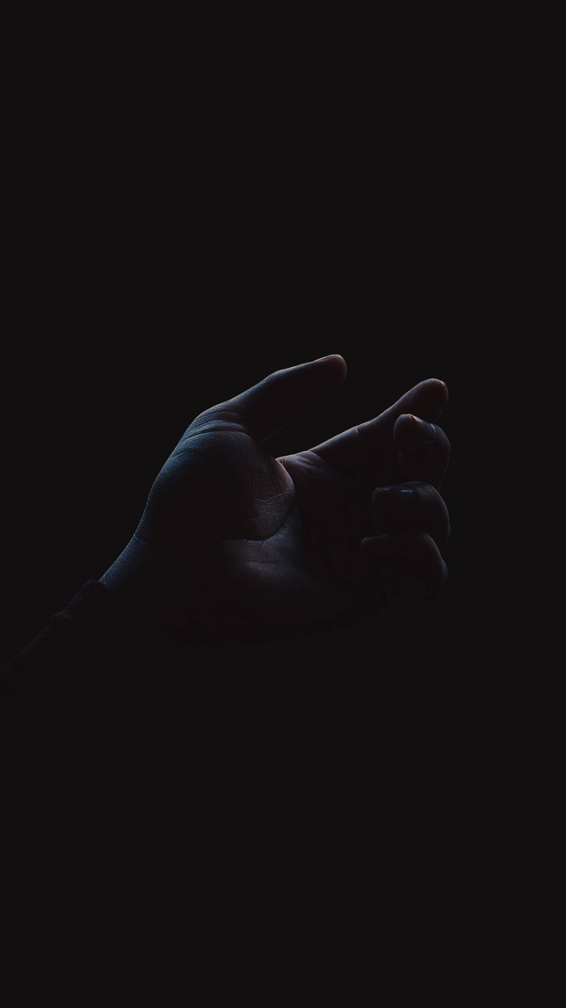 手機 桌布 壁紙 — 一隻手從黑暗中浮現，手指微微彎曲，在黑色虛空中被柔和的藍光照亮。