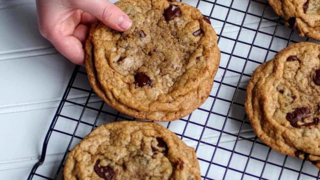 720p Cookies 桌布 壁紙 — 一隻手從黑色金屬架上拿起一塊暖巧克力餅乾，旁邊還有其他餅乾在白色表面上冷卻。