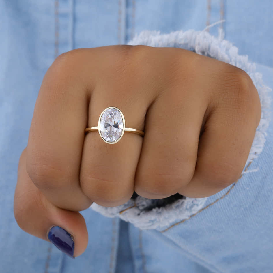 Ring 桌布 壁紙 — 一隻手戴著金戒指，戒指上有橢圓形切割鑽石，戴在無名指上，穿著破洞牛仔布。