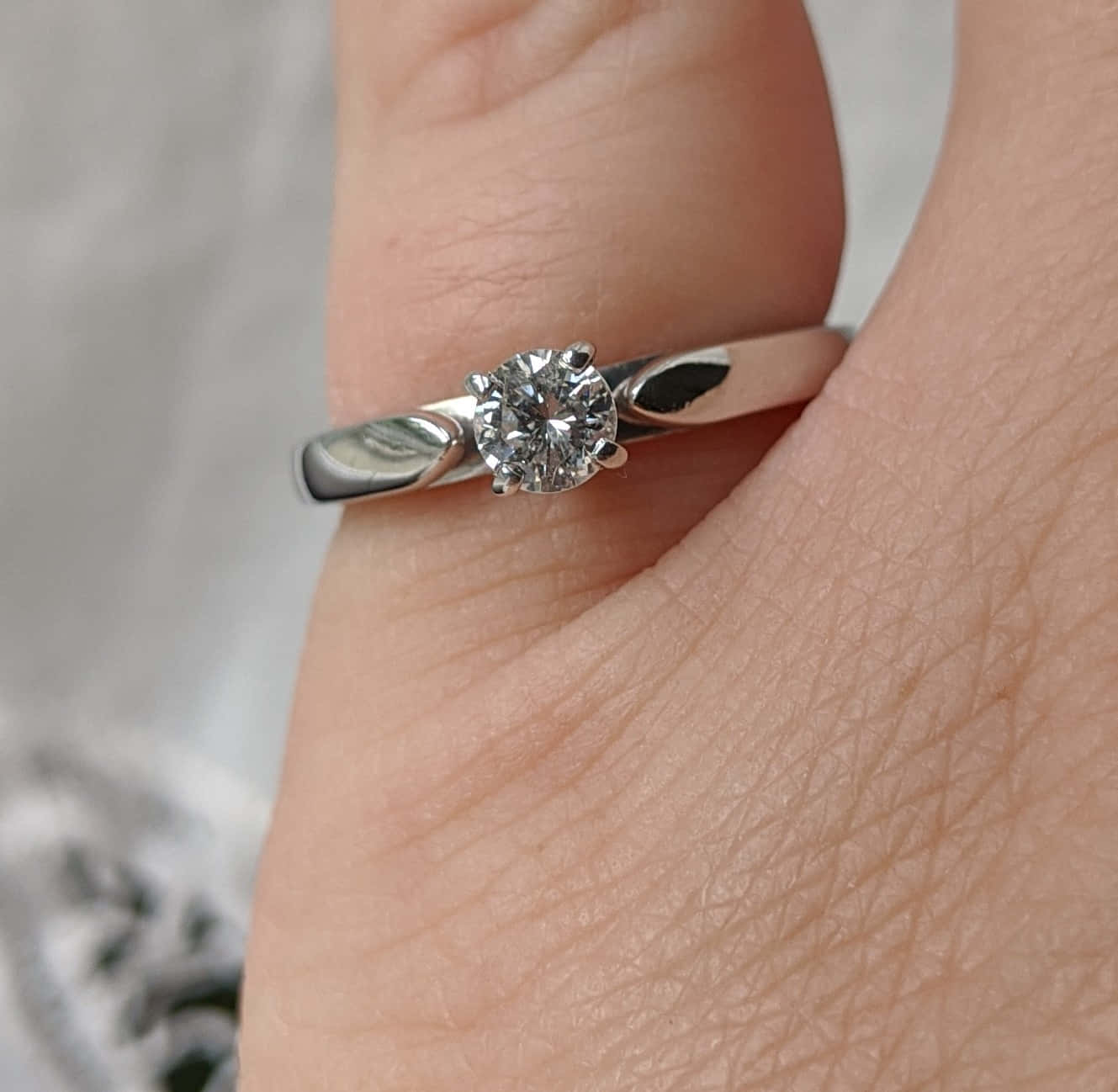 rings 桌布 壁紙 — 一隻手戴著銀色單鑽訂婚戒指的特寫，戒指帶有簡約的指環。