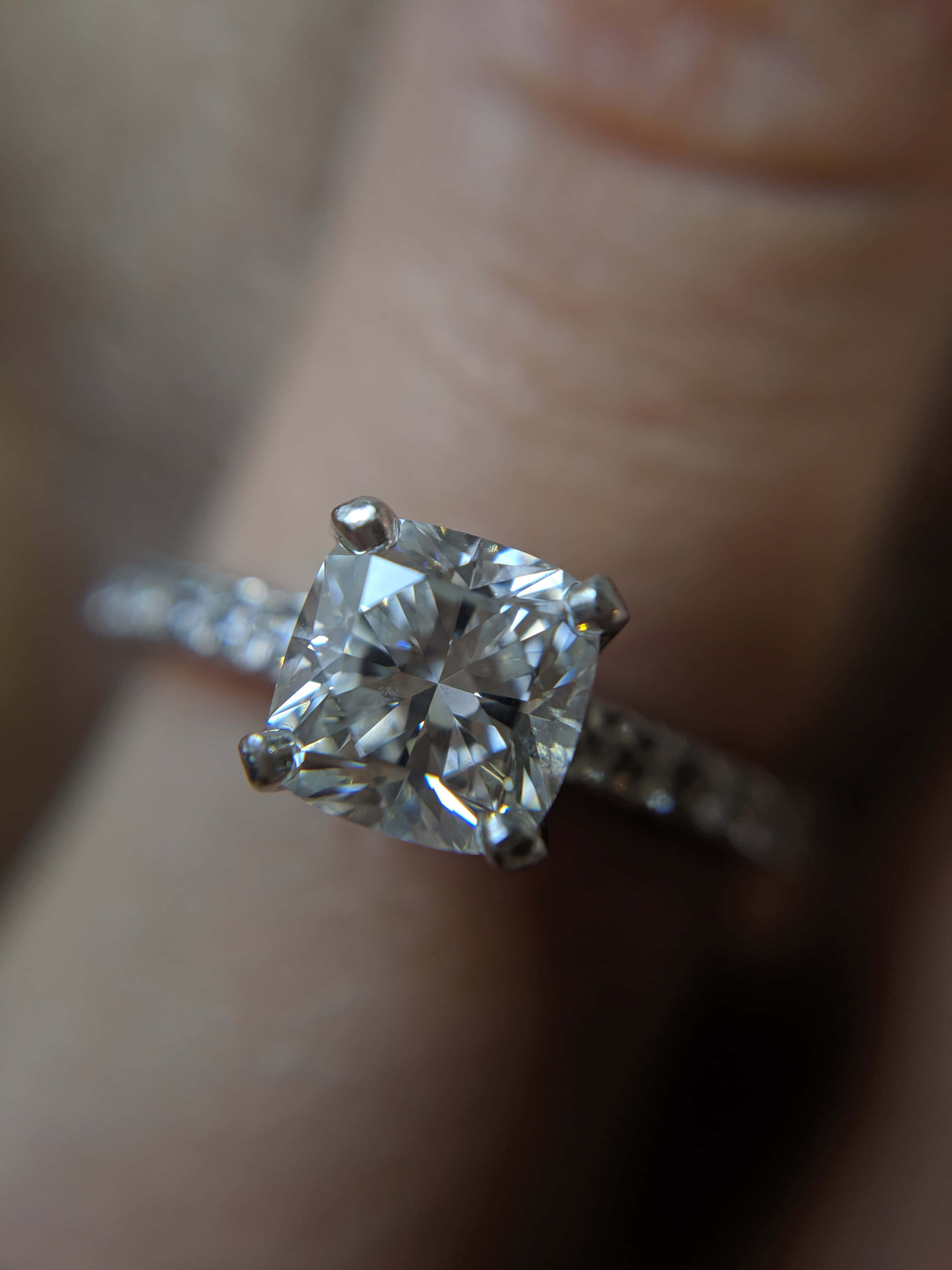 rings 桌布 壁紙 — 一隻手戴著閃爍的方形切割鑽石訂婚戒指，帶有密鑲戒指環的近距離特寫。