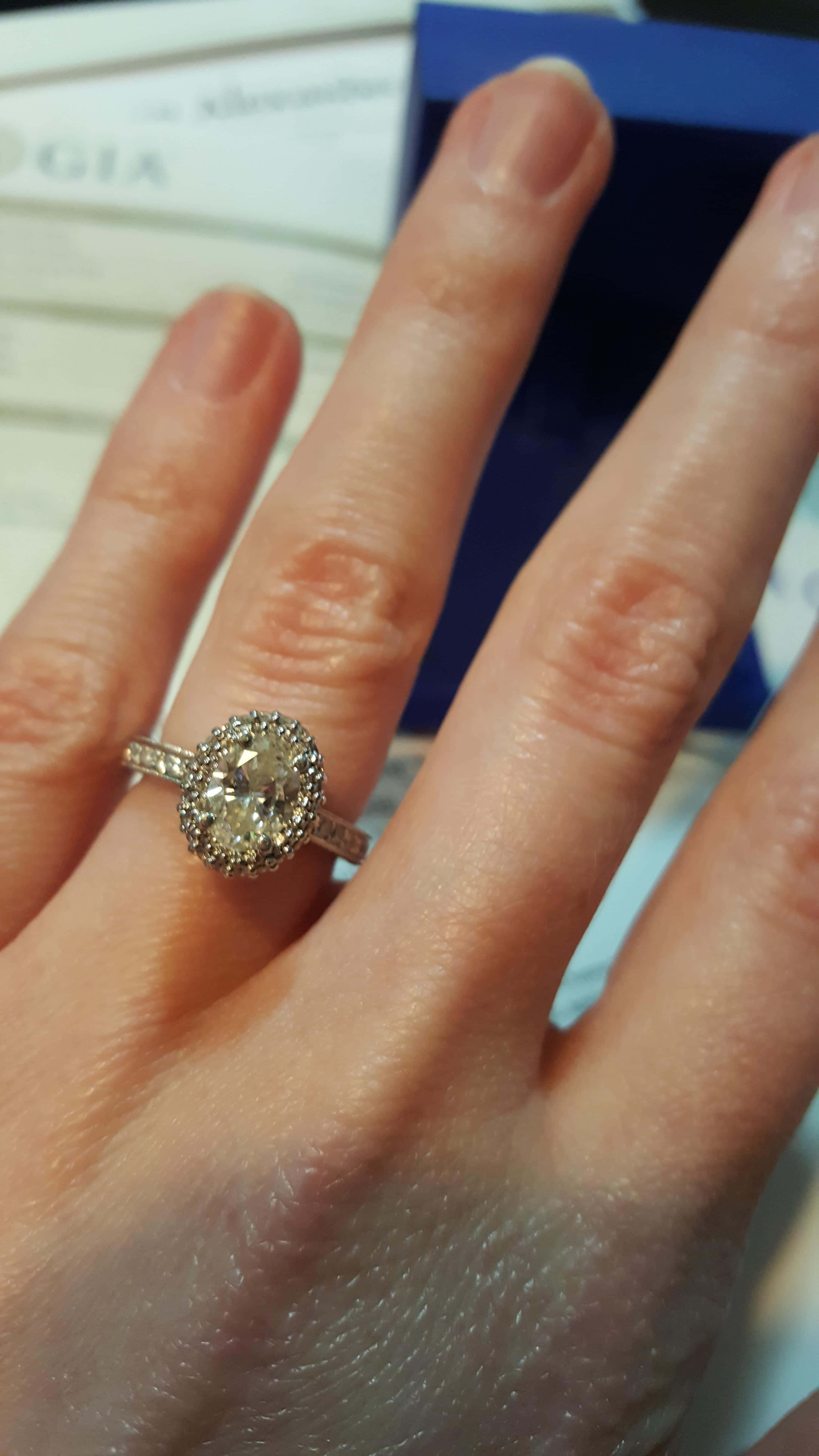 rings 桌布 壁紙 — 一隻手戴著閃閃發光的鑽石光環訂婚戒指的特寫，背景可見GIA證書。