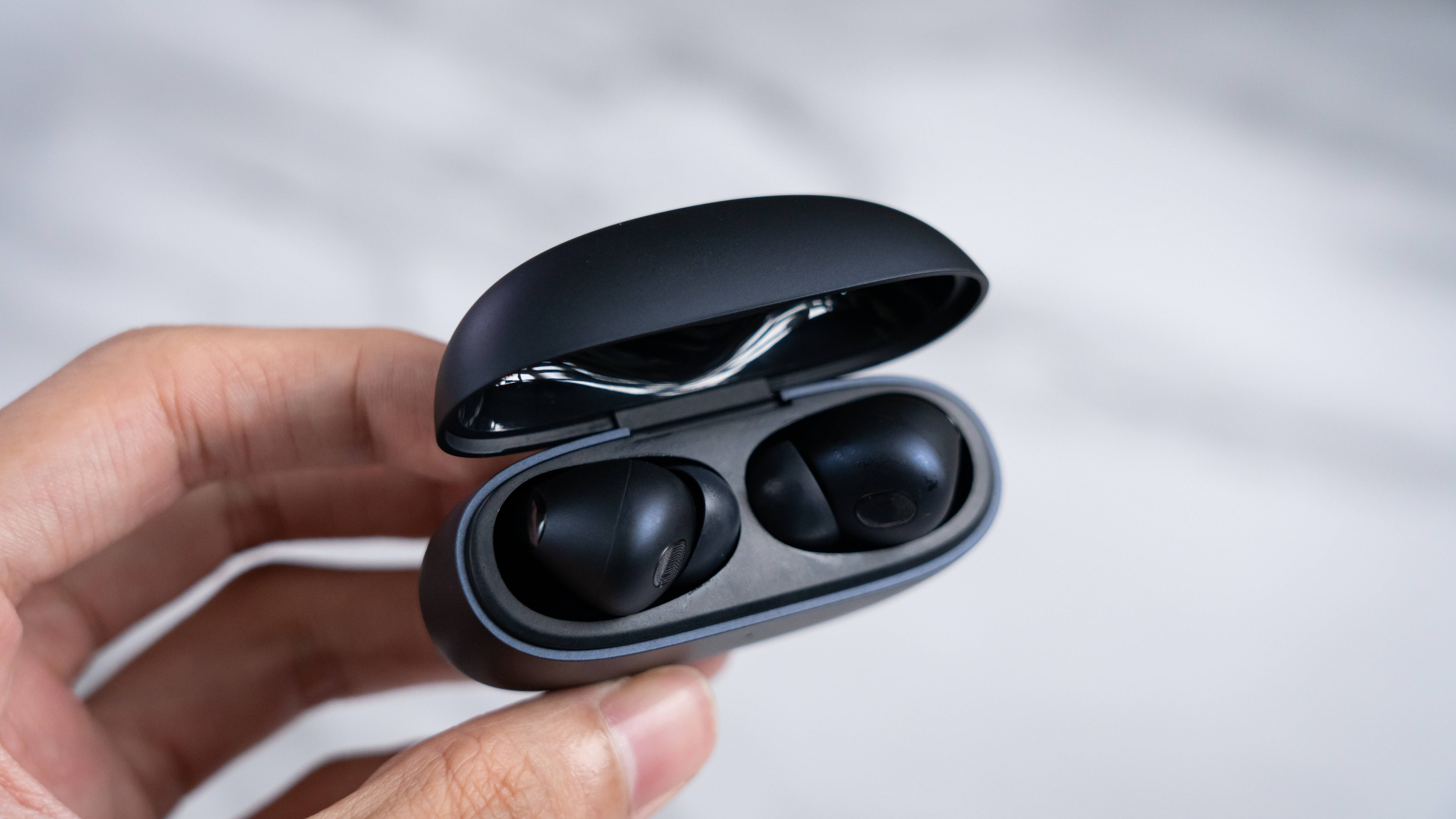 Xiaomi 桌布 壁紙 — 一隻手打開一個時尚的黑色無線耳機盒，露出兩個霧面黑色耳機，背景是柔和的白色大理石。