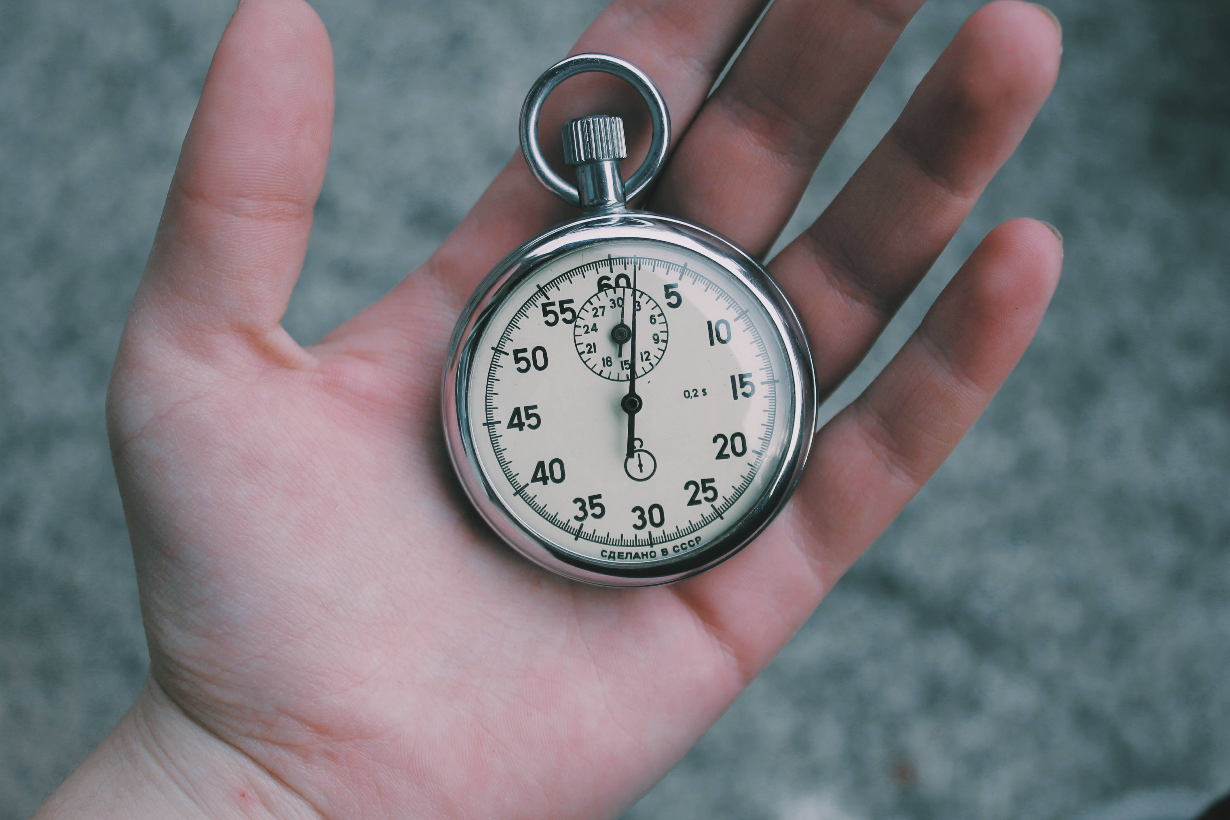 sexy time 桌布 壁紙 — 一隻手托著一個復古銀色計時碼錶，帶有奶油色錶盤，背景是模糊的灰色。