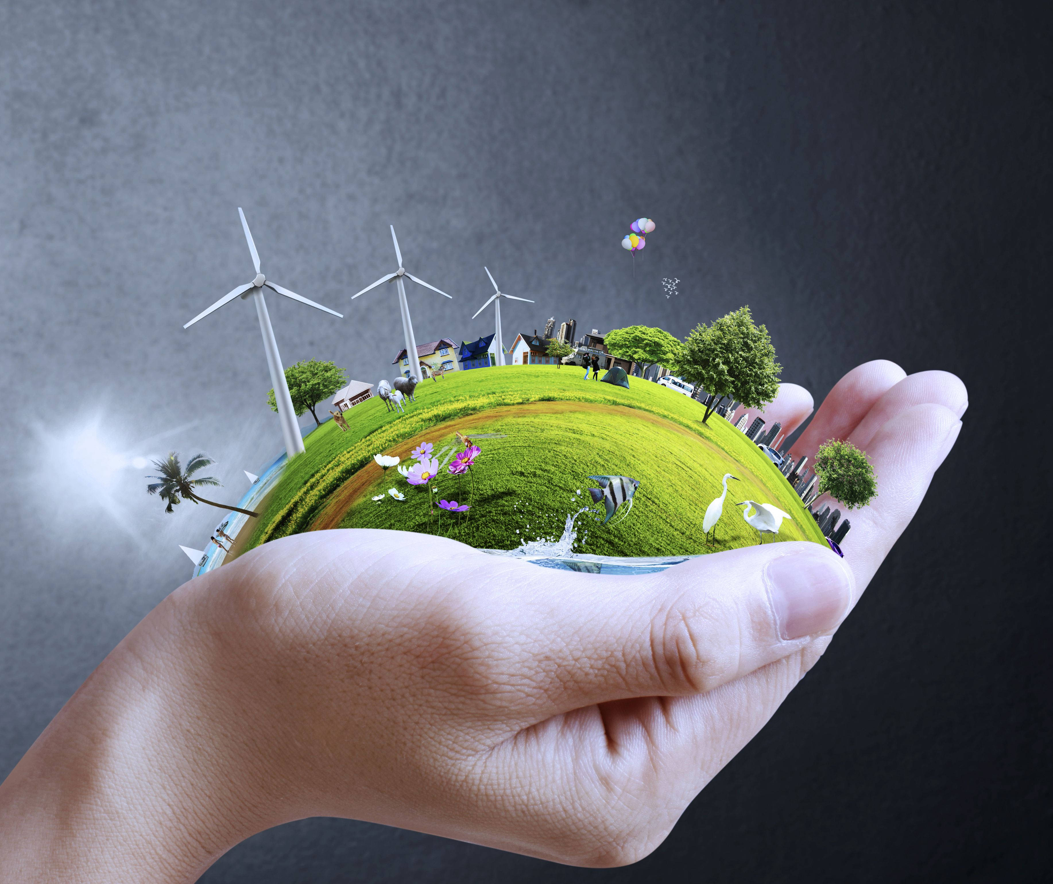 Earth Day 桌布 壁紙 — 一隻手托著一個微型地球儀，上面展示風力渦輪機、綠色田野和野生動物，背景為深灰色。