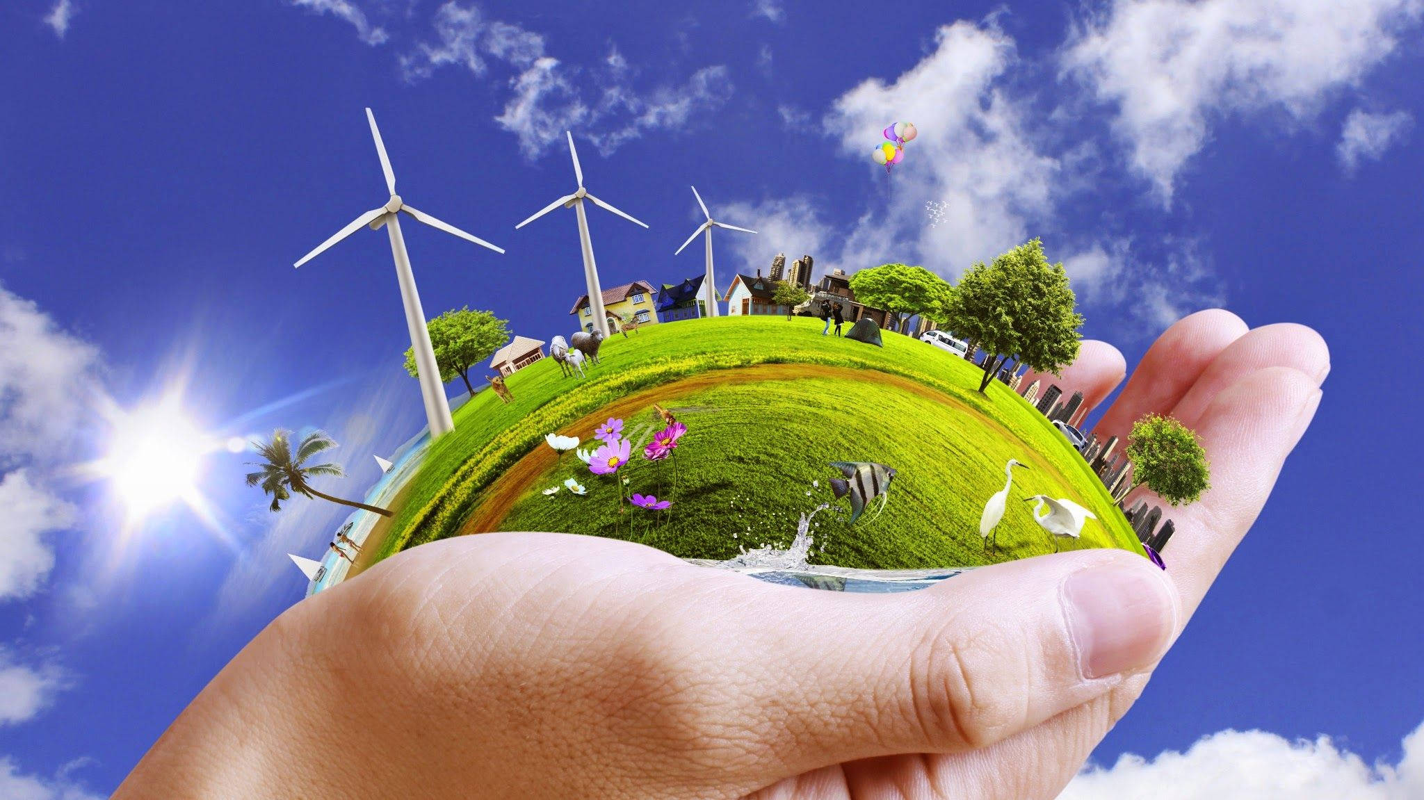 Earth Day 桌布 壁紙 — 一隻手托著一個微型地球儀，上面顯示風力發電機、房屋、樹木和野生動物，背景是明亮的藍天和陽光。