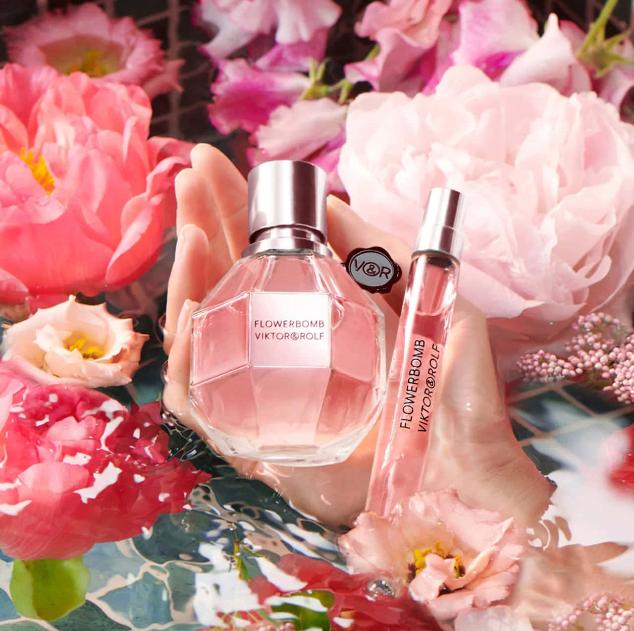 Spring Perfume 桌布 壁紙 — 一隻手托著粉紅色的Viktor&Rolf Flowerbomb香水瓶和旅行裝小瓶，周圍是水中茂盛的粉紅色和紅色牡丹。