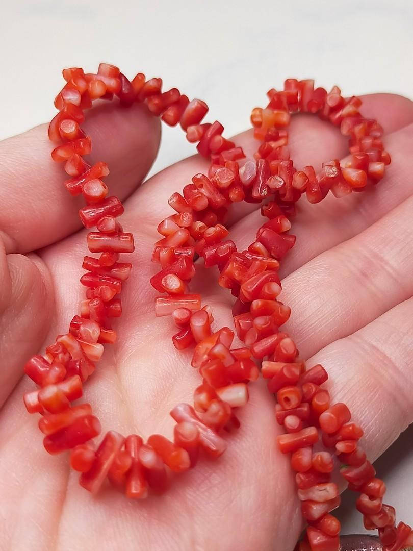 coral 桌布 壁紙 — 一隻手托著鮮紅色珊瑚珠，形狀像小圓柱和管子，背景是柔和的白色。