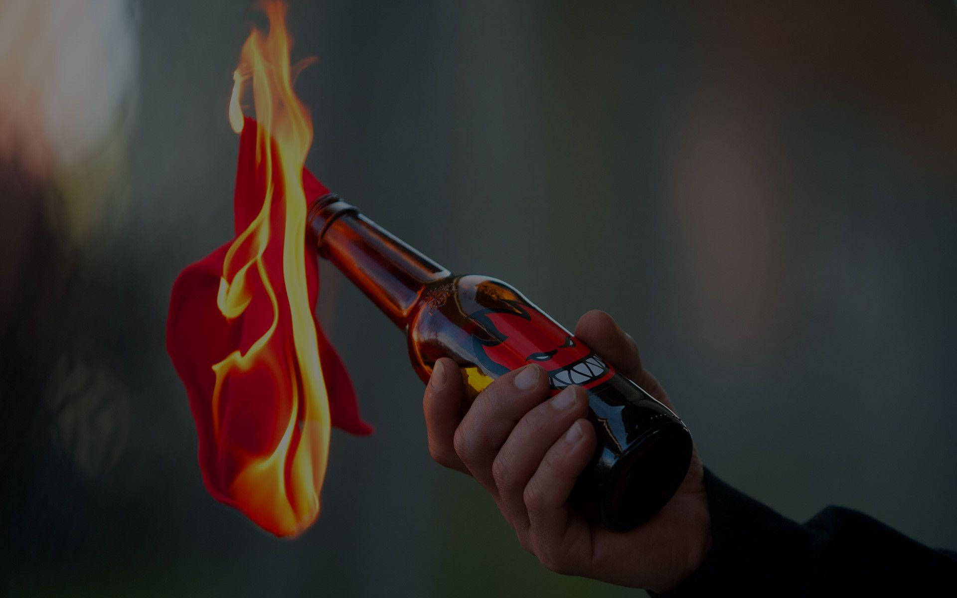 標誌 桌布 壁紙 — 一隻手抓住一個瓶子，瓶子中噴出鮮豔的火焰，在黑暗模糊的背景上投射出溫暖的光芒。