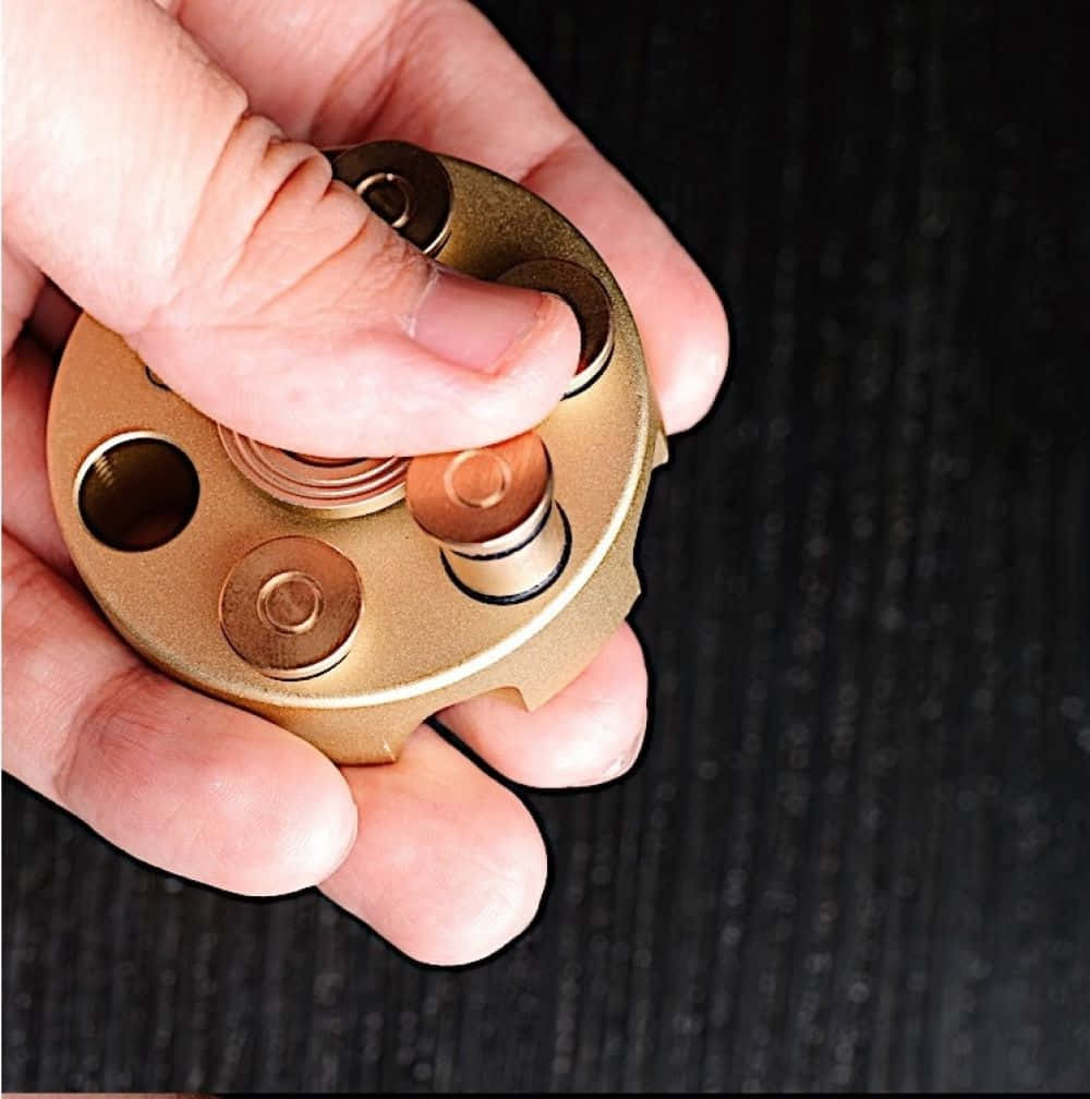 Fidget 桌布 壁紙 — 一隻手抓住一個黃銅色的指尖陀螺，背景為深色紋理。