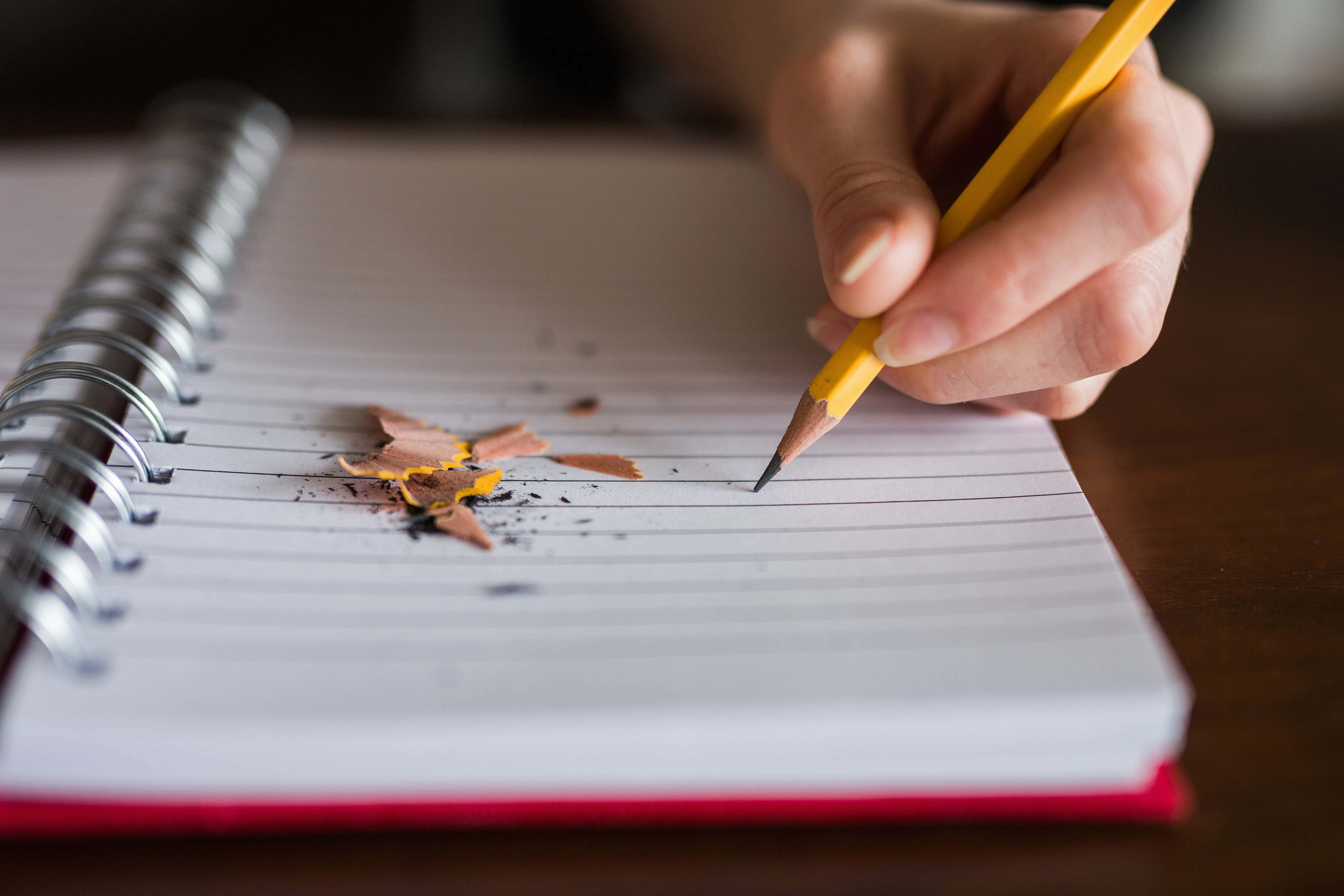 pencil 桌布 壁紙 — 一隻手抓住一支黃色鉛筆，懸在散落木屑的橫線筆記本紙上。