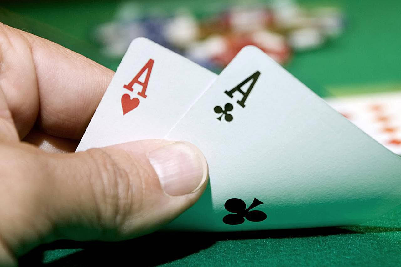 Playing Cards 桌布 壁紙 — 一隻手抓住兩張紅心和梅花Ace，放在綠色撲克桌上，背景有模糊的籌碼。