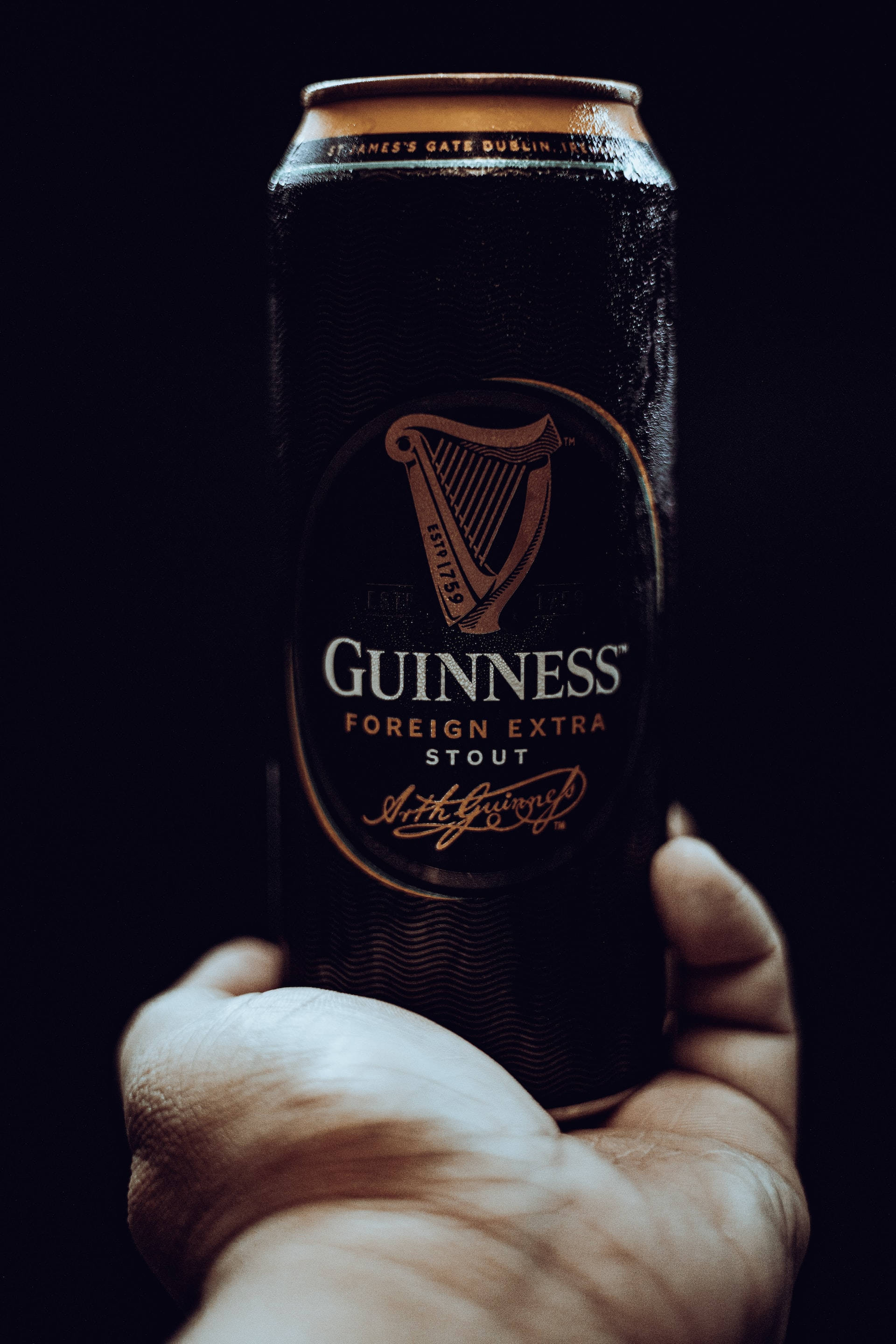 Beer 桌布 壁紙 — 一隻手抓住冰凍的健力士 Foreign Extra Stout 罐裝啤酒，背景為純黑色，燈光效果強烈。