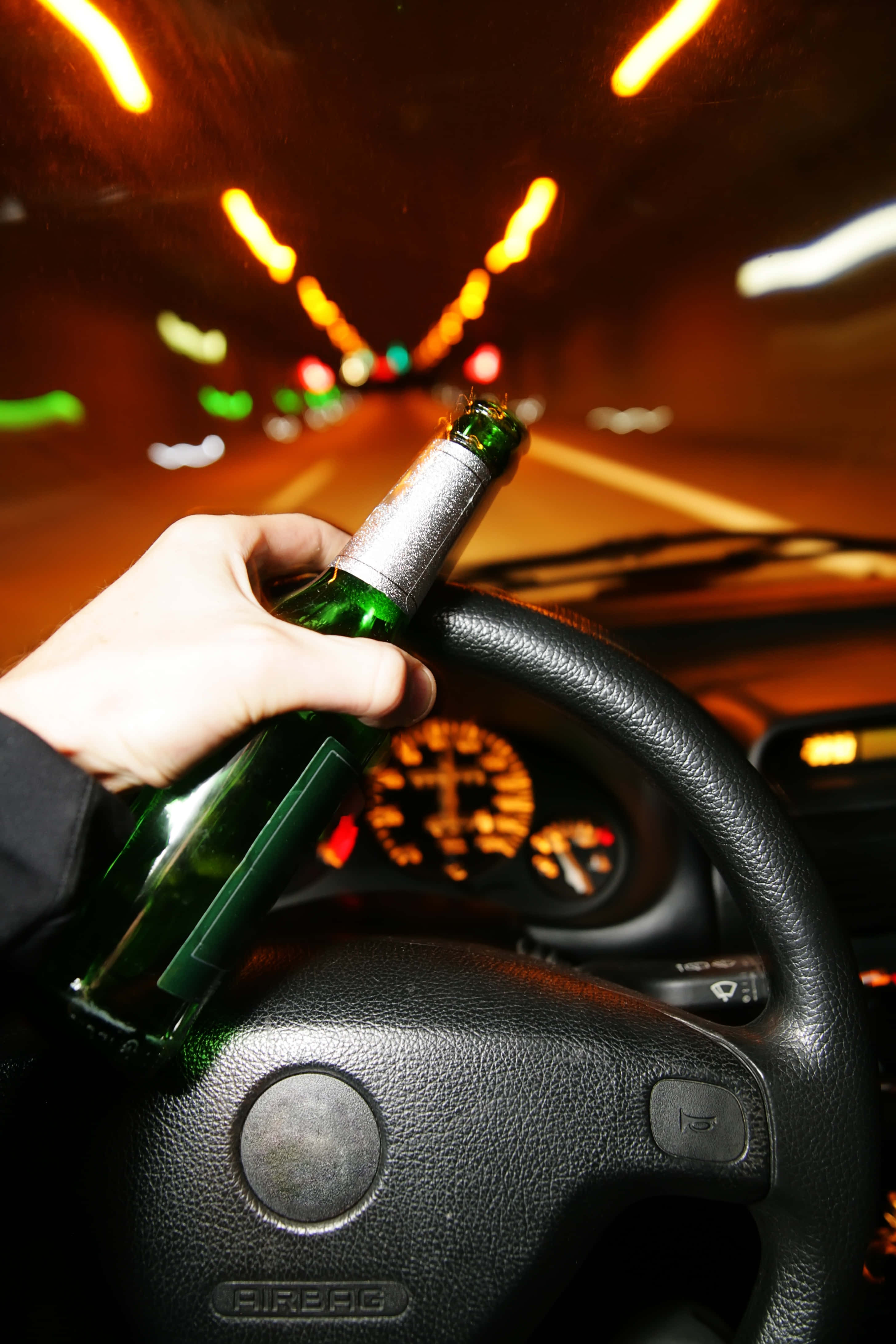 Drunk 桌布 壁紙 — 一隻手抓住汽車方向盤上的綠色啤酒瓶，模糊的隧道燈光以溫暖的橙色色調掠過。
