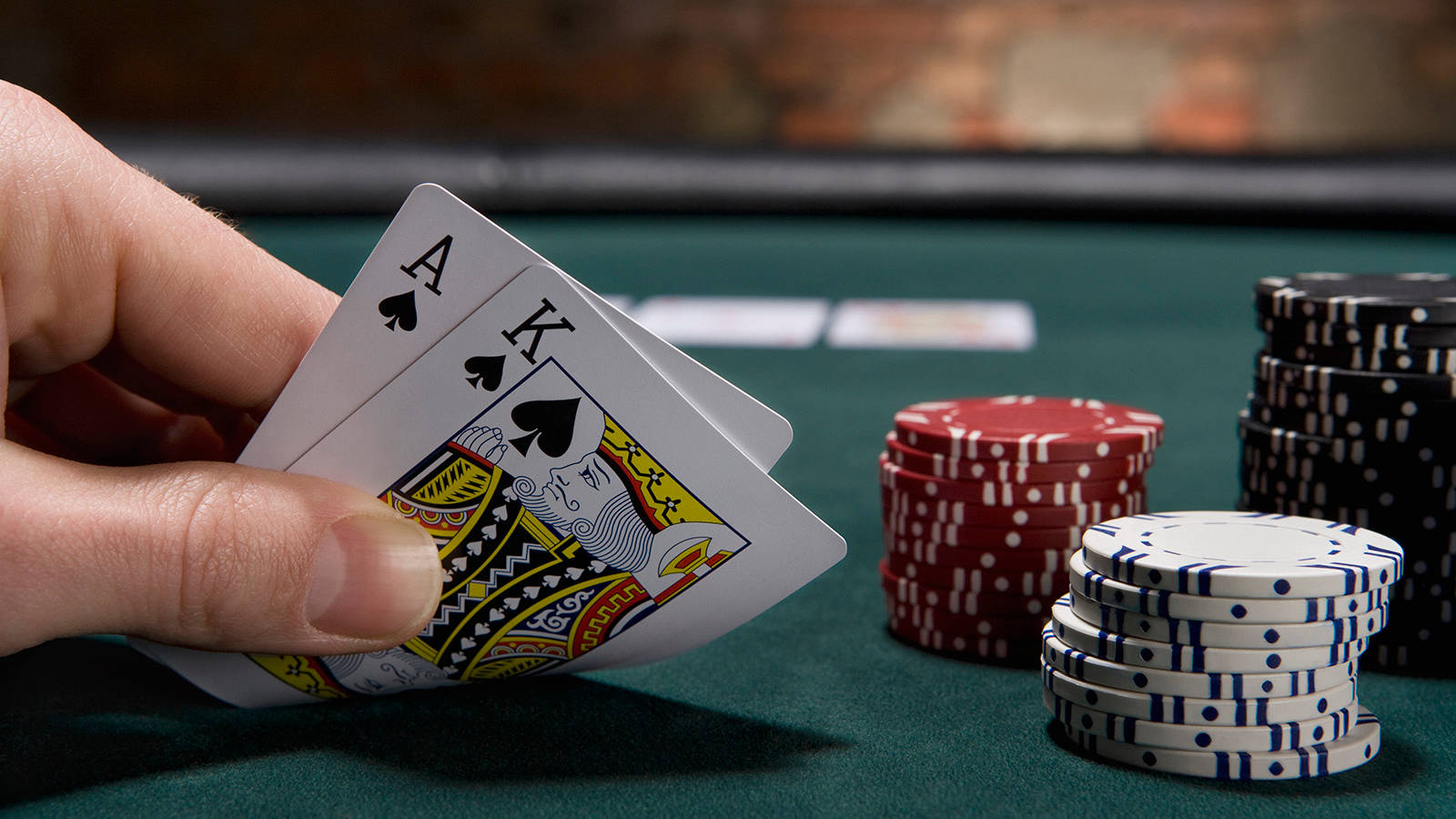 Poker Table 桌布 壁紙 — 一隻手抓住黑桃A和K，放在綠色賭桌上，桌上有紅色、白色和黑色的籌碼堆。
