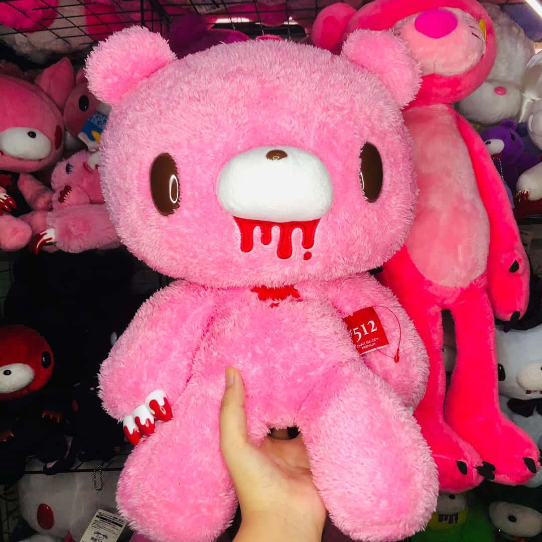 gloomy bear 桌布 壁紙 — 一隻手拎著一個毛茸茸的粉紅色泰迪熊，嘴巴和爪子滴著血，周圍是類似恐怖主題的毛絨動物。