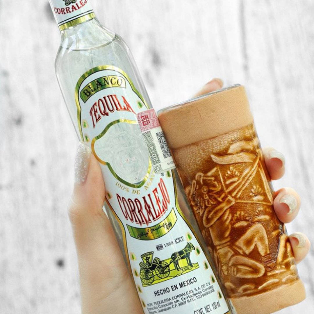 bottle 桌布 壁紙 — 一隻手拿著Corralejo blanco龍舌蘭酒瓶和一個雕刻木杯，背景是淺色木材。