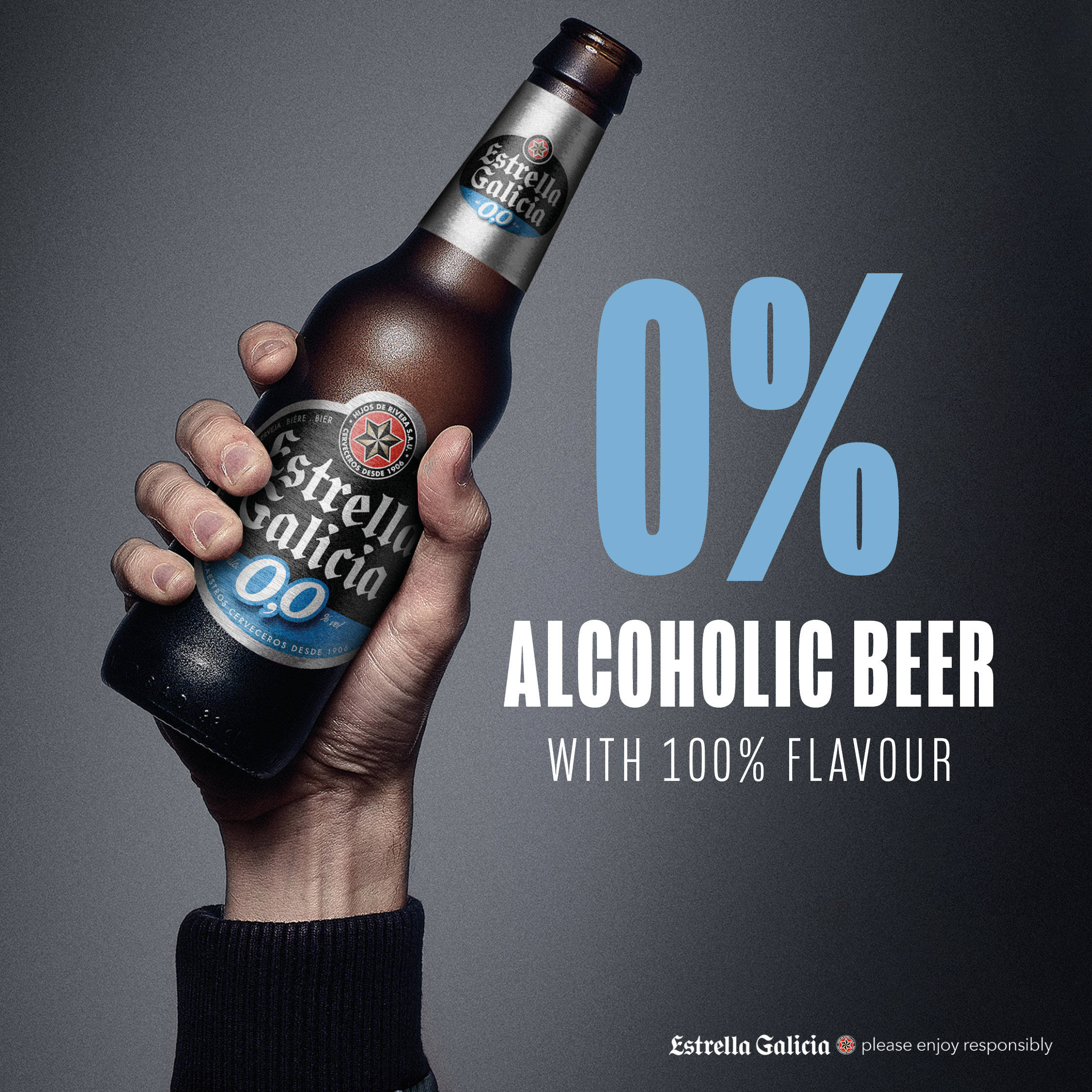 Beer 桌布 壁紙 — 一隻手拿著Estrella Galicia 0.0無酒精啤酒的棕色瓶子，背景為深灰色，粗體藍色和白色文字宣告「0% 無酒精啤酒 100% 風味」。
