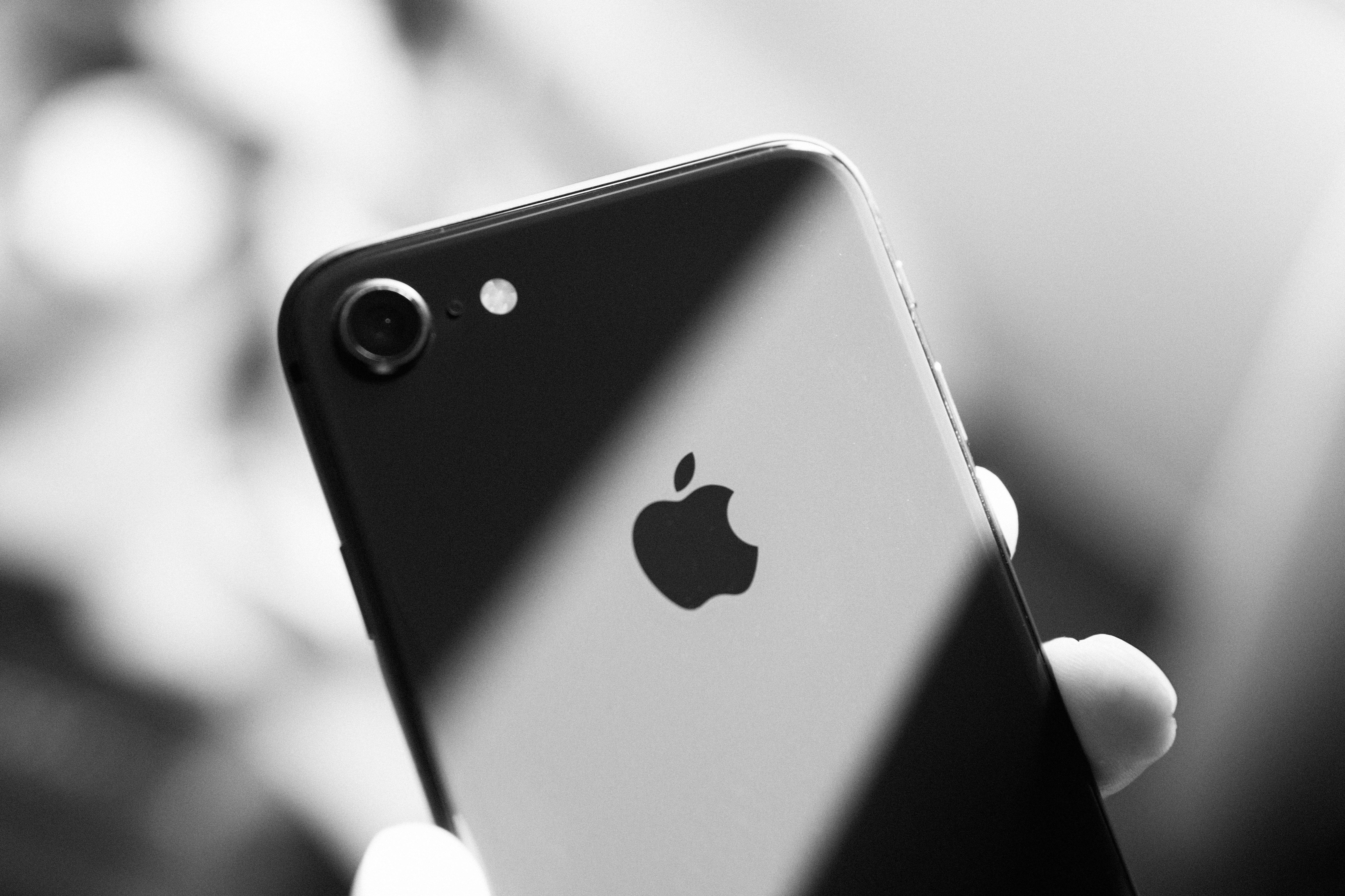 iPhone 8 桌布 壁紙 — 一隻手拿著iPhone的黑白特寫，Apple標誌和相機清晰可見。
