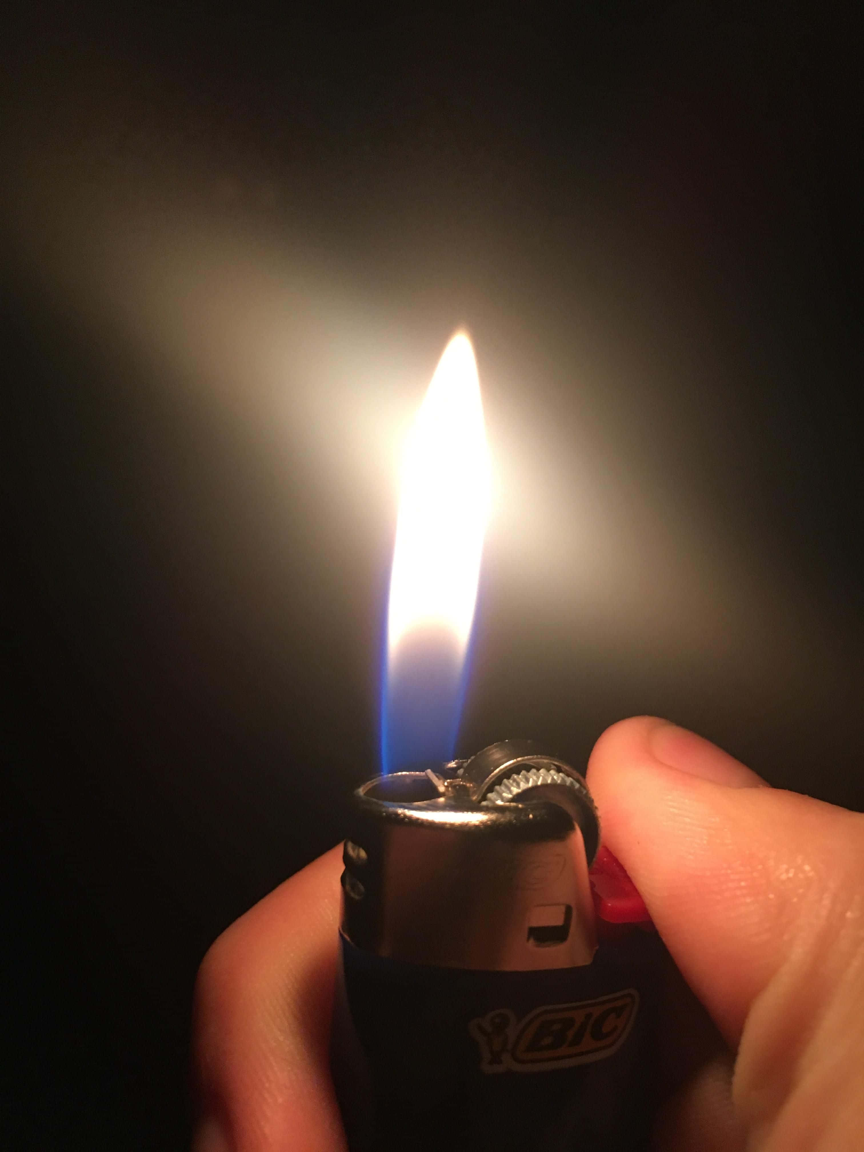 lighter 桌布 壁紙 — 一隻手拿著一個BIC打火機，明亮的藍白色火焰在黑暗背景中發光。