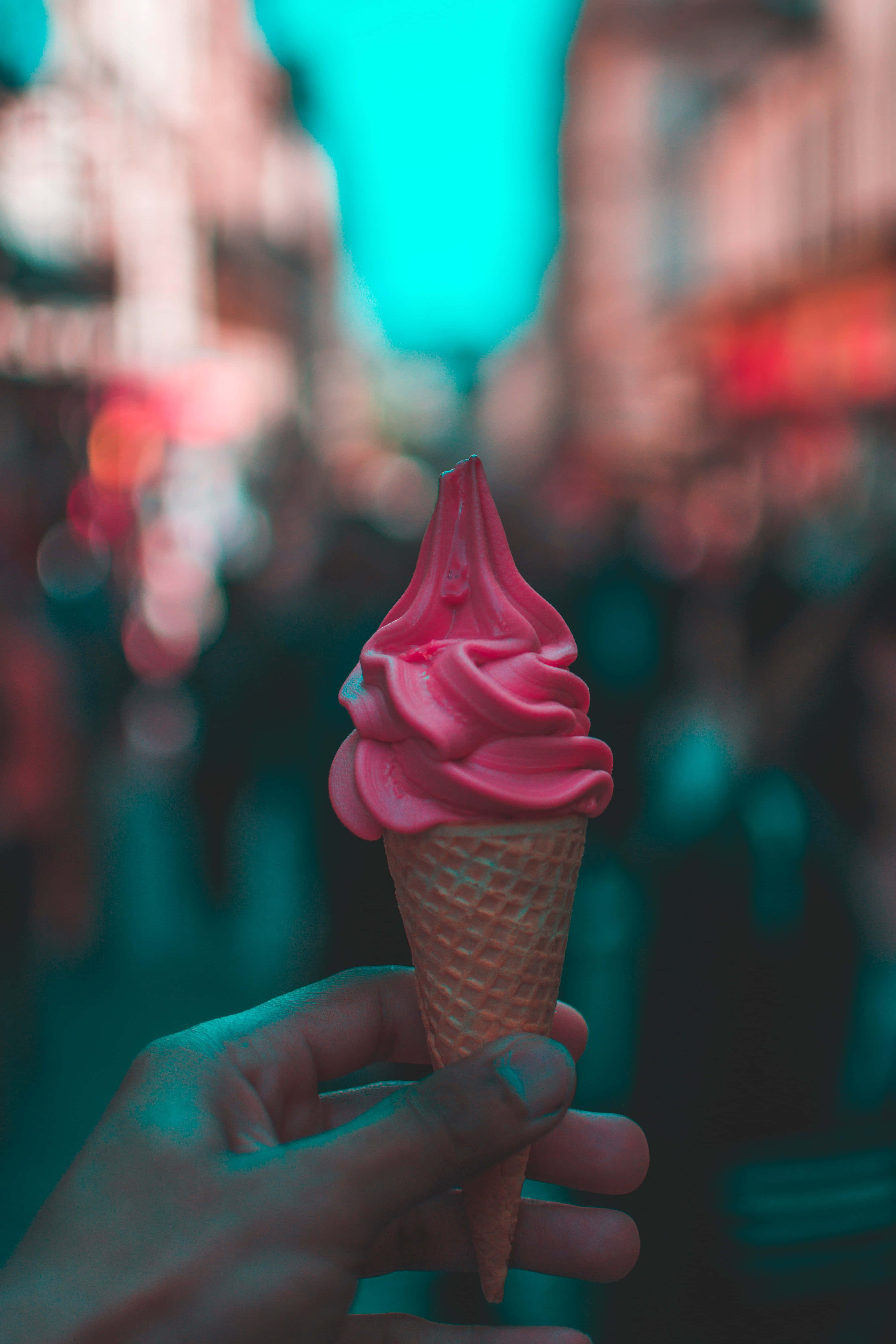 Ice Cream 桌布 壁紙 — 一隻手拿著一個充滿活力的粉紅色軟冰淇淋甜筒，背景是模糊的霓虹燈城市夜景。