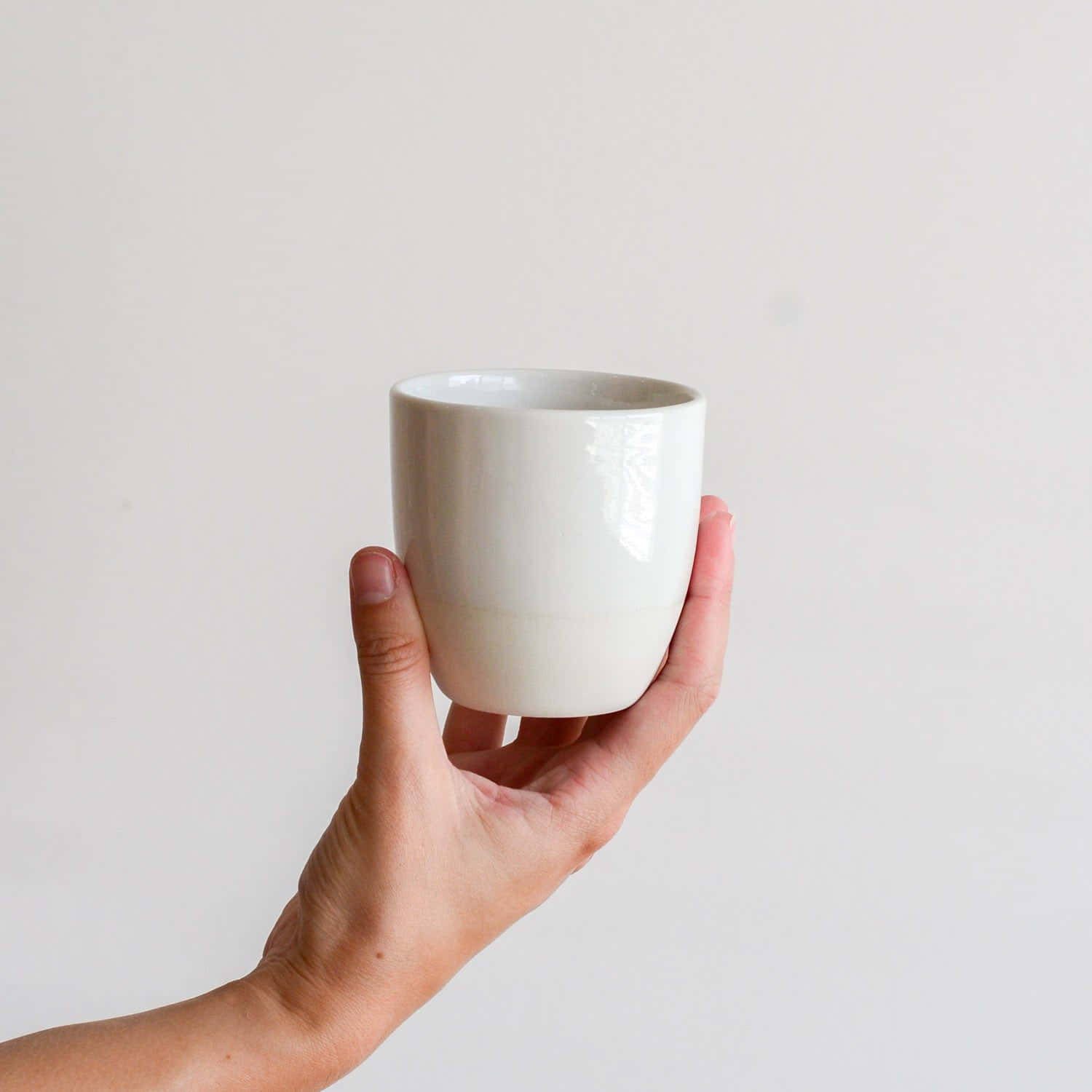 Ceramic 桌布 壁紙 — 一隻手拿著一個光滑的白色陶瓷杯，背景是純淺灰色。