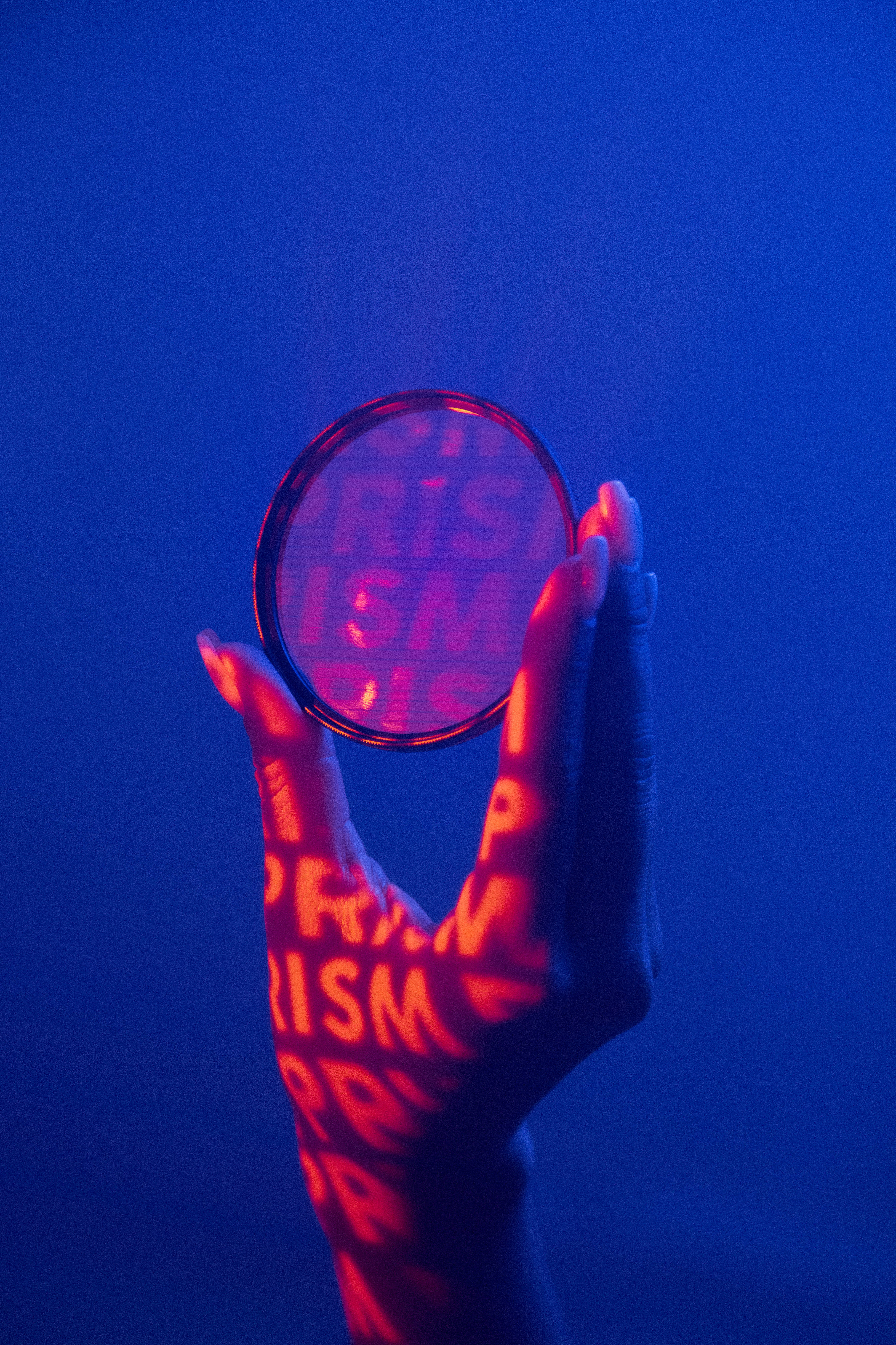 Prism 桌布 壁紙 — 一隻手拿著一個圓形棱鏡，在深藍色背景上將發光的紅色「PRISM」文字投射到皮膚上。