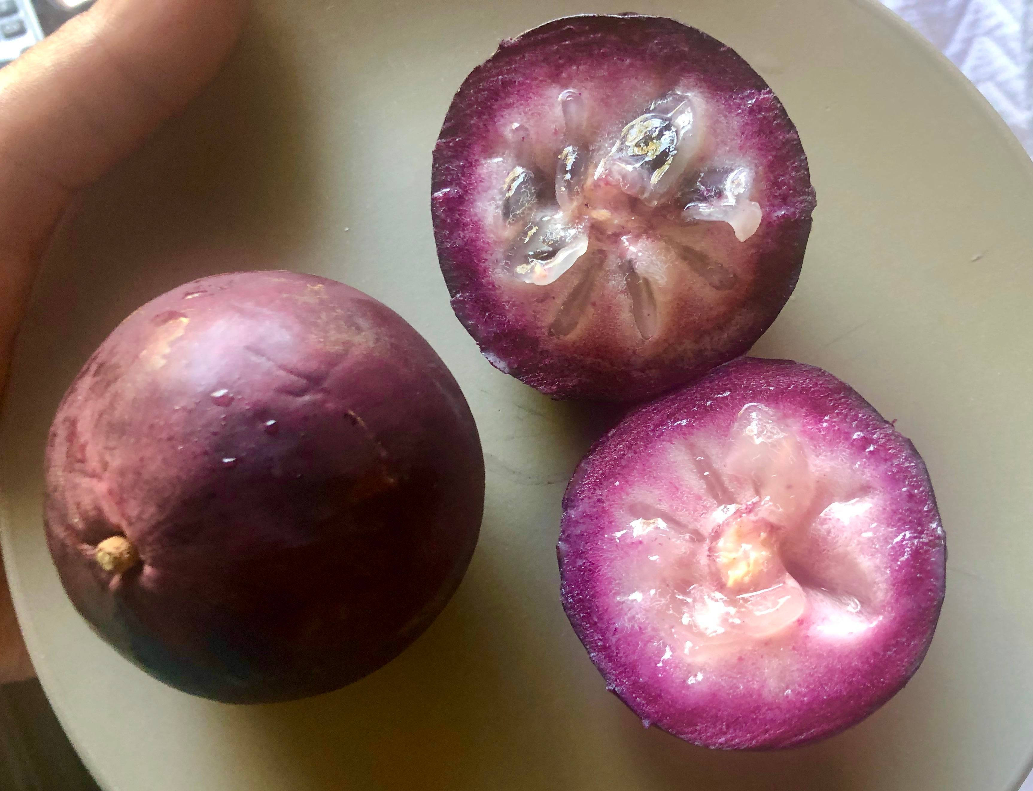 Fruit 桌布 壁紙 — 一隻手拿著一個完整的紫色山竹，旁邊有兩半，露出多汁的粉紅色果肉和白色種子，放在淺色盤子上。