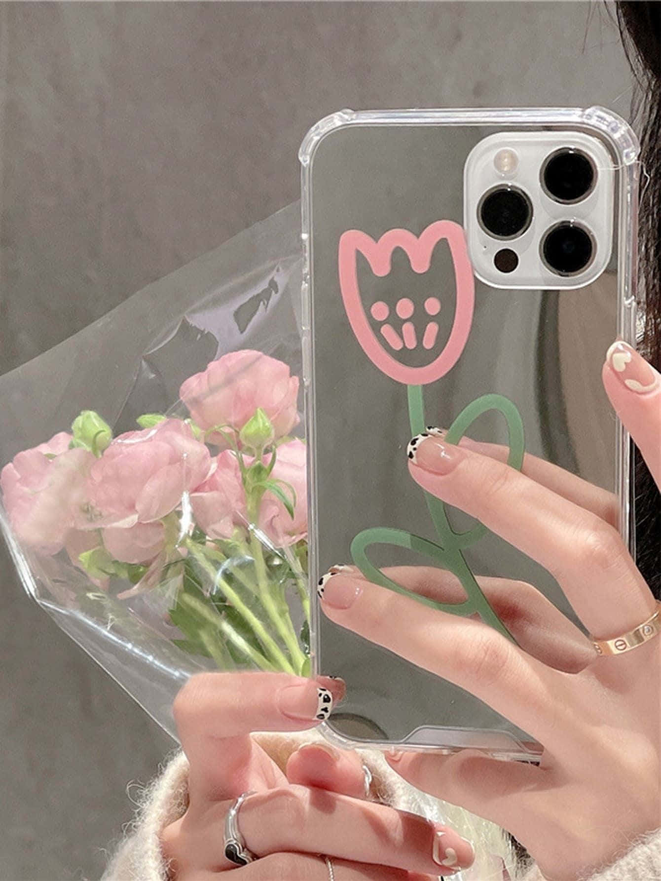 iPhone 12 桌布 壁紙 — 一隻手拿著一個帶有粉紅色鬱金香設計的透明手機殼，同時握著一束粉紅色的花。