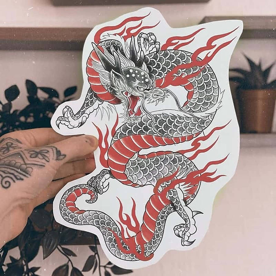 Japanese Dragon Tattoo 桌布 壁紙 — 一隻手拿著一個帶有詳細鱗片和爪子的火紅黑色紋身風格龍貼紙，背景是模糊的室內環境。