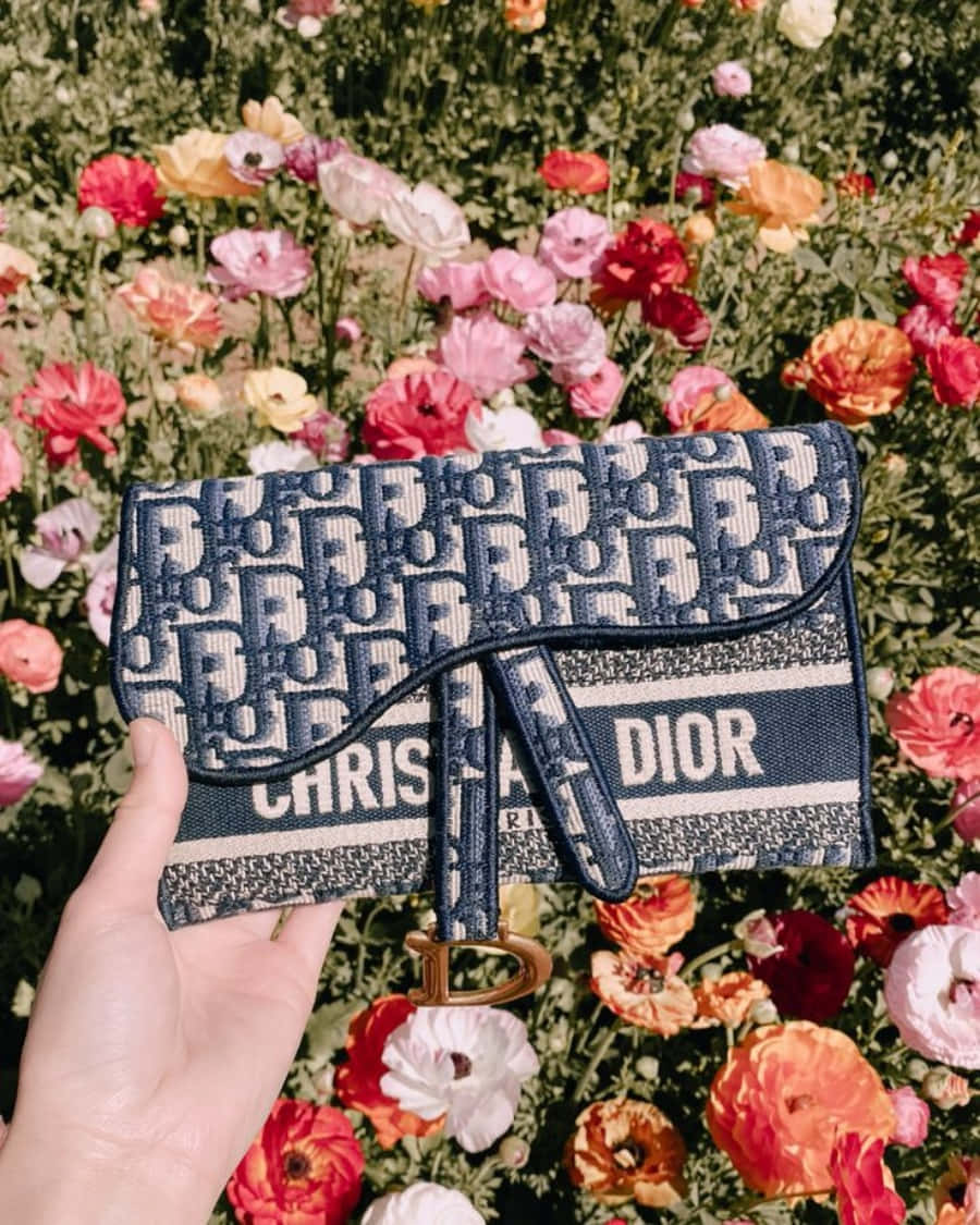 Dior 動態 桌布 壁紙 — 一隻手拿著一個帶有重複標誌的藍色Dior錢包，背景是陽光下色彩繽紛的罌粟花田。