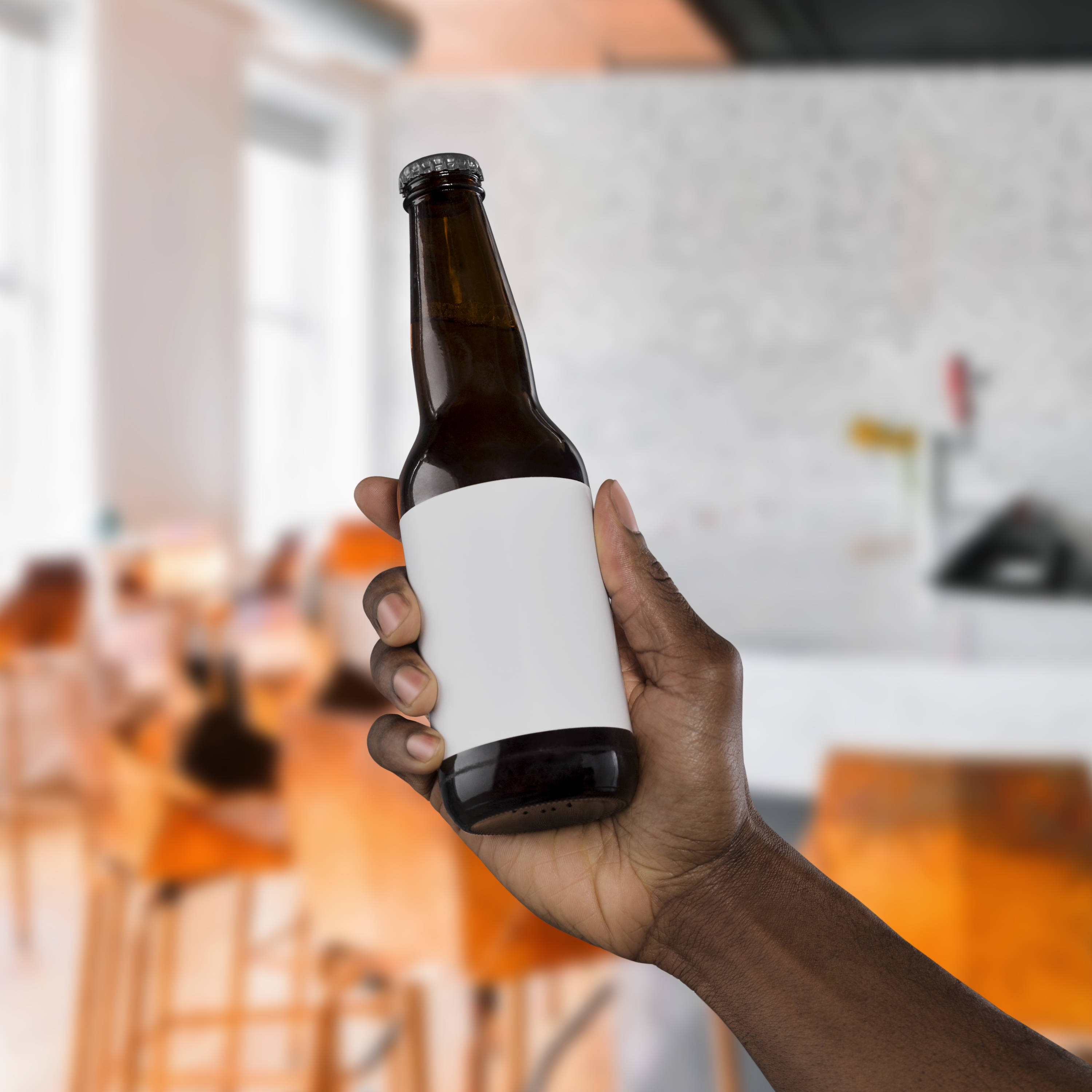 Beer 桌布 壁紙 — 一隻手拿著一個棕色啤酒瓶，帶有空白白色標籤，背景是模糊的現代咖啡館。