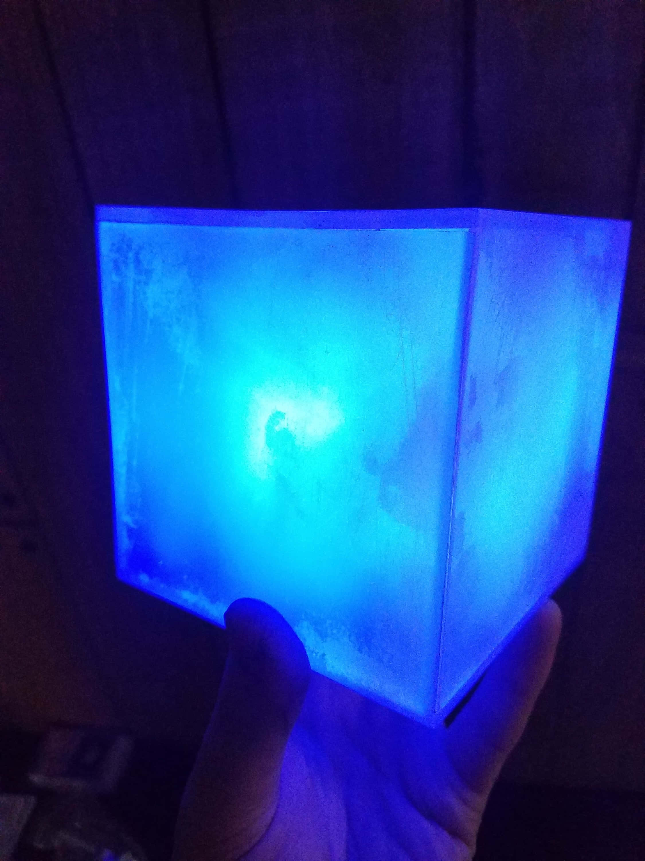 Space Stone 桌布 壁紙 — 一隻手拿著一個發光的藍色半透明立方體，在深色木質背景上發出柔和的光線。