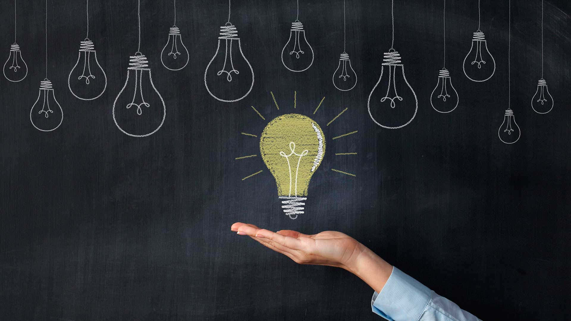 Light Bulb 桌布 壁紙 — 一隻手拿著一個發光的黃色粉筆畫燈泡，對著黑板，上面掛著其他輪廓燈泡。