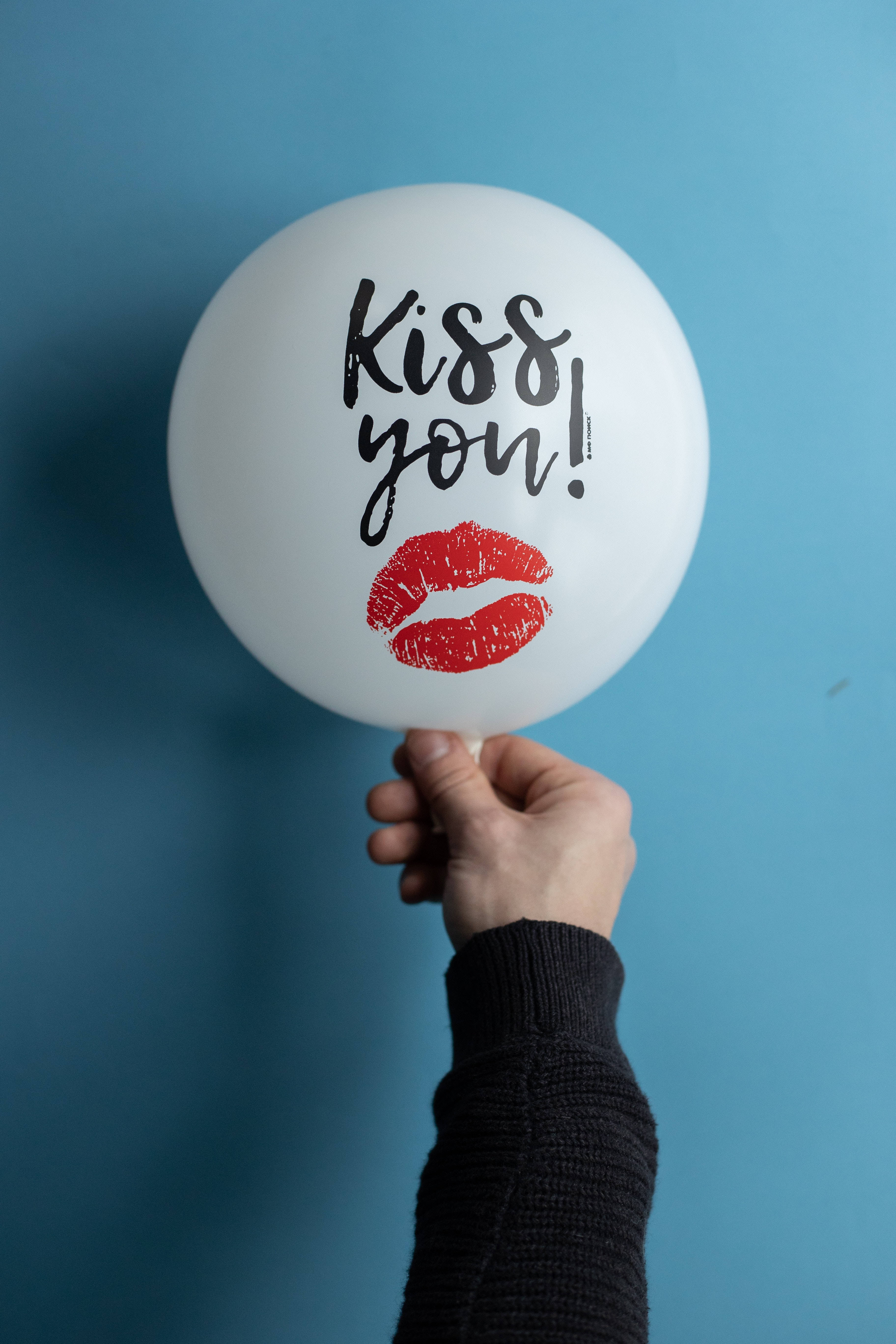 Cute Blue 桌布 壁紙 — 一隻手拿著一個白色氣球，上面有 'Kiss you!' 的文字和紅色唇印，背景為純藍色。