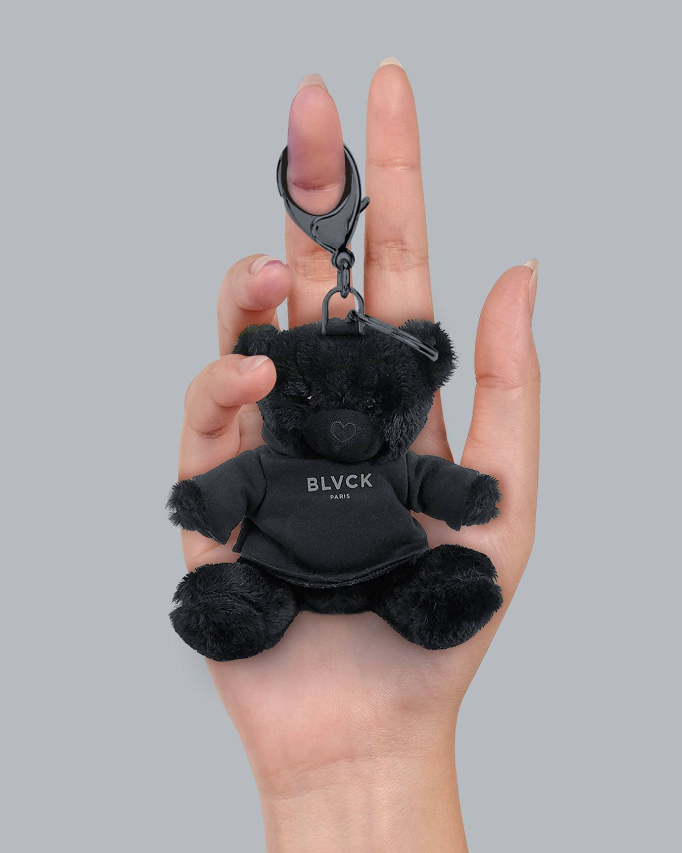 Blvck Paris 桌布 壁紙 — 一隻手拿著一個穿著品牌襯衫的小黑熊鑰匙圈，背景是純灰色。