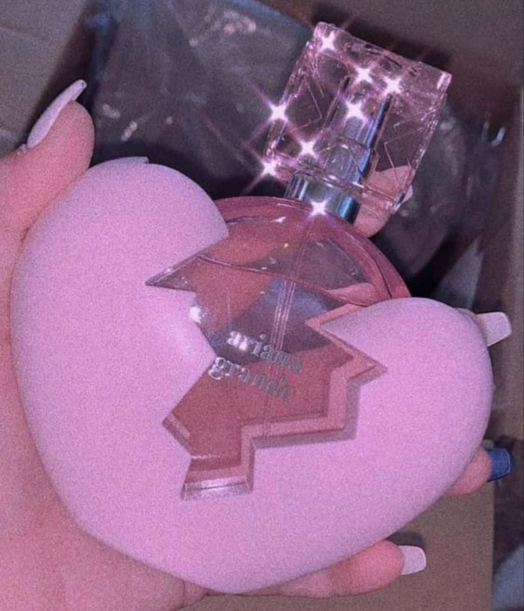 Boujee Aesthetic 桌布 壁紙 — 一隻手拿著一個粉紅色心形香水瓶，帶有破碎設計和閃閃發光的瓶蓋。