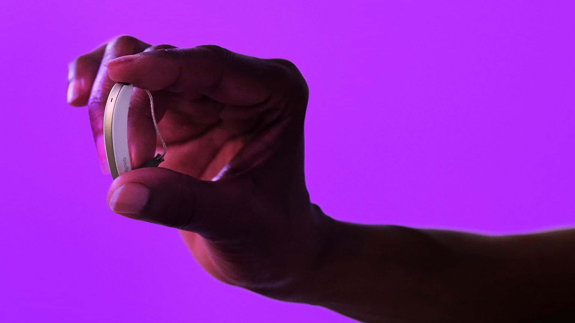 aids 桌布 壁紙 — 一隻手拿著一個細小的銀色助聽器，背景是鮮豔的紫色。
