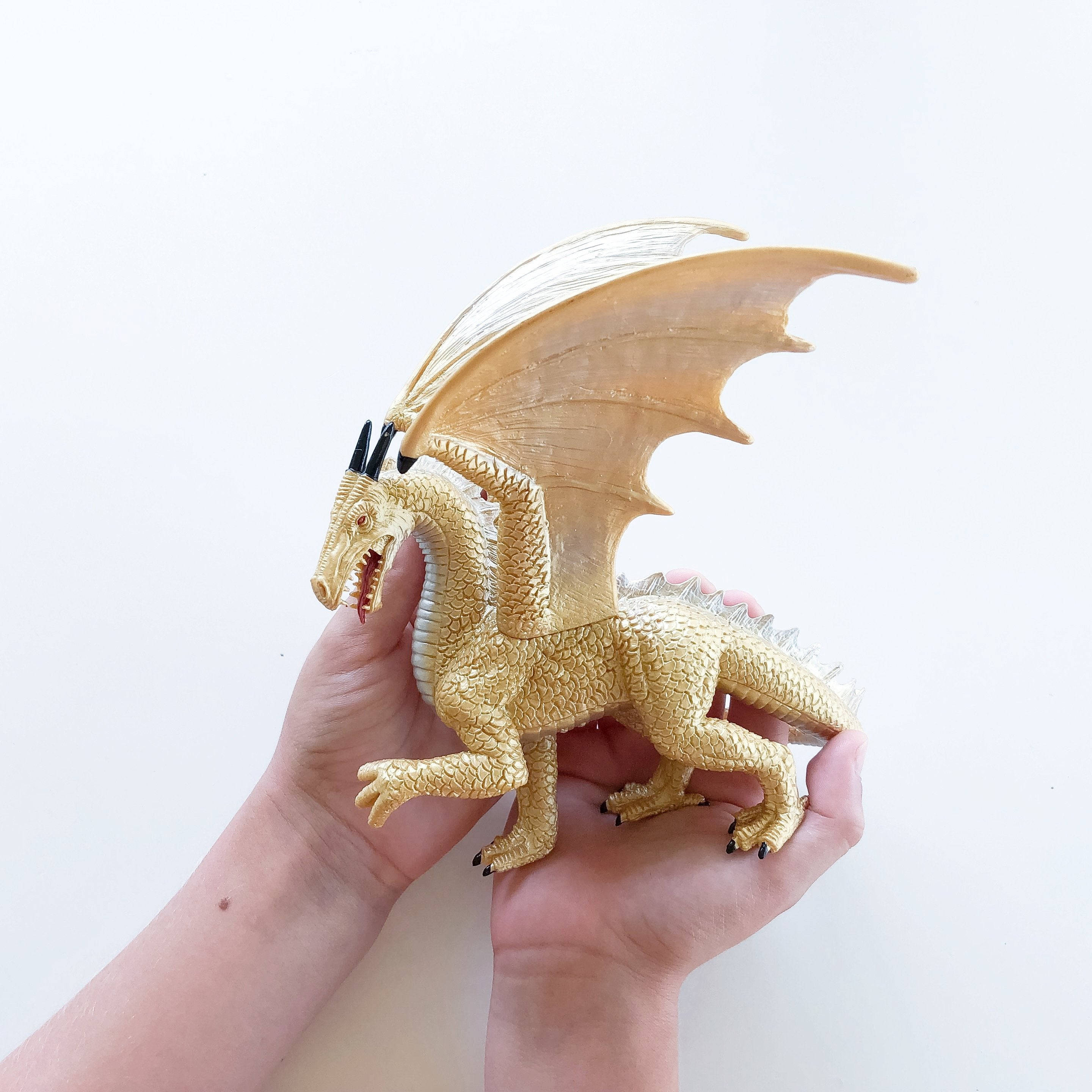 Gold Dragon 桌布 壁紙 — 一隻手拿著一個細節豐富的金色龍玩具，翅膀展開，背景是純白色。