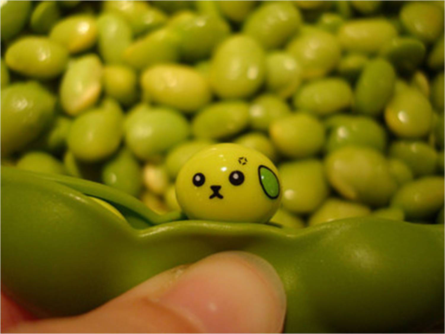 Vegetables 桌布 壁紙 — 一隻手拿著一個綠色豌豆莢，其中一顆卡通臉的豌豆在許多相似的豌豆中探出頭來。