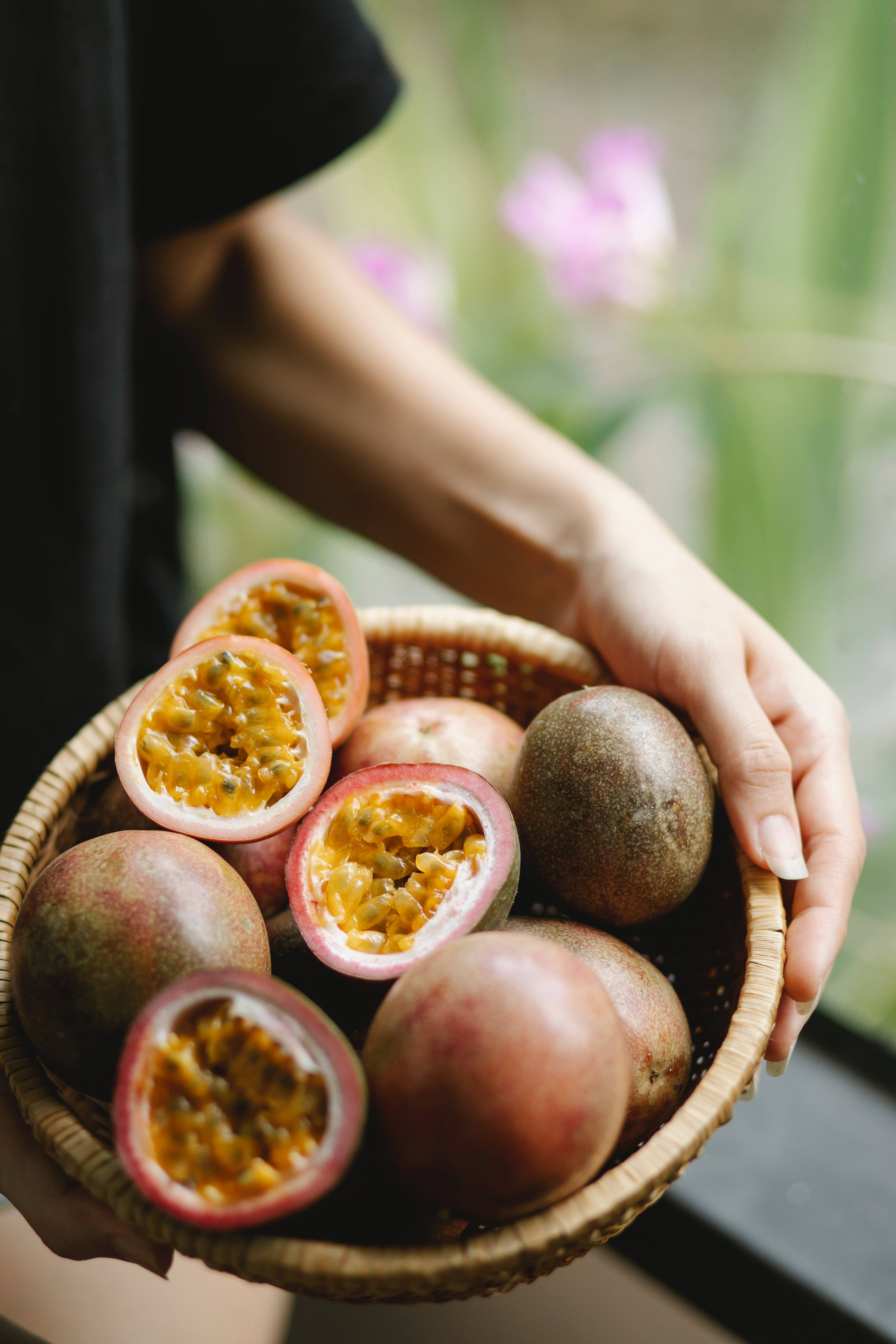 Fruits 桌布 壁紙 — 一隻手拿著一個編織籃，裡面裝滿成熟的百香果，有些切開，露出多汁的橙色果肉，背景是柔和模糊的花園。