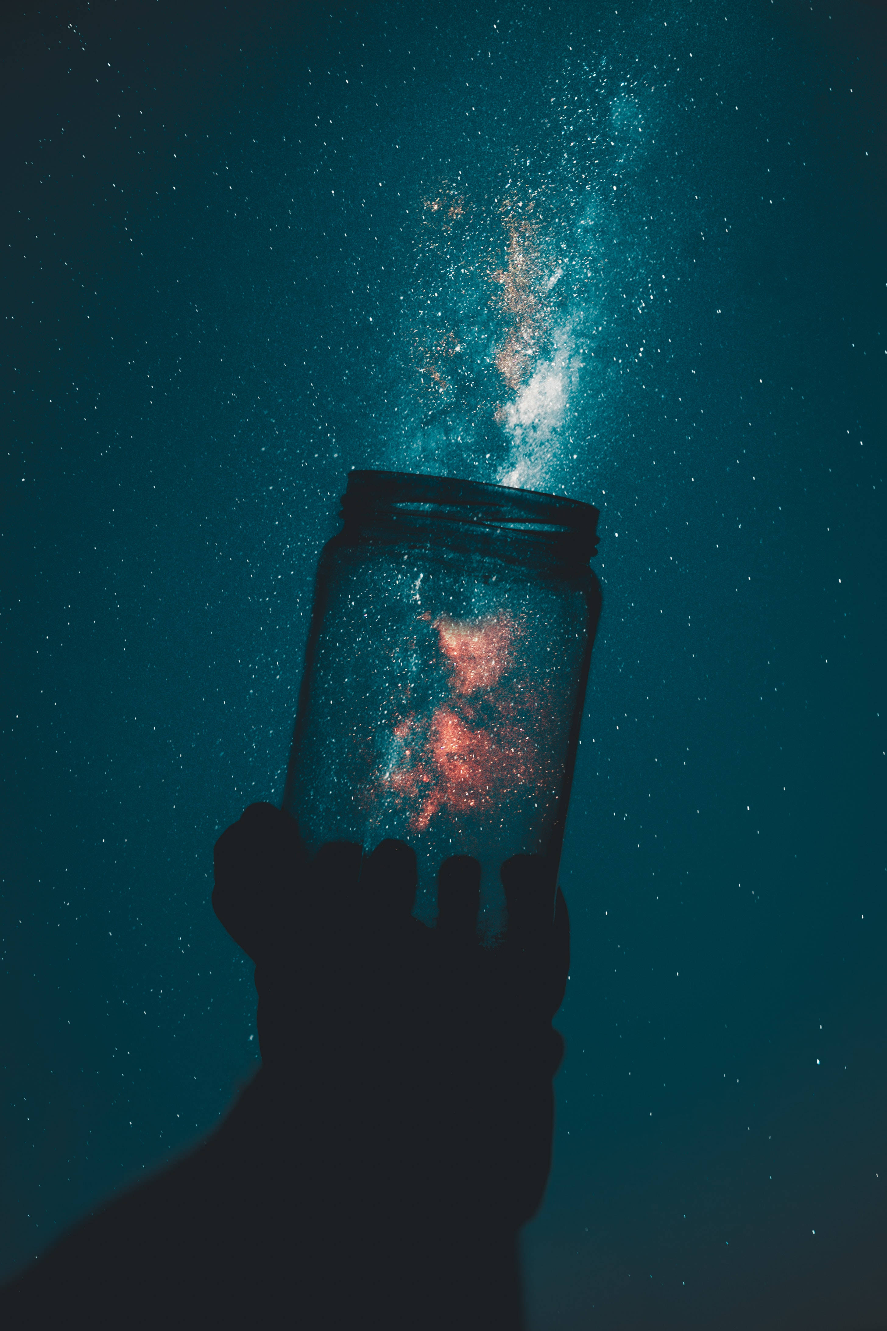 外太空 桌布 壁紙 — 一隻手拿著一個罐子，裡面裝滿了閃閃發光的宇宙塵埃，背景是繁星點點的藍綠色夜空。