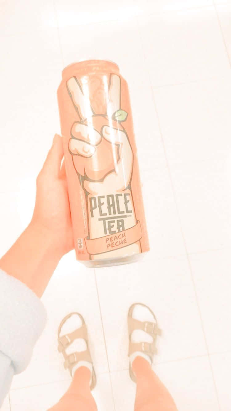 Peachy Aesthetic 桌布 壁紙 — 一隻手拿著一個蜜桃味和平茶罐，上面有和平標誌設計，背景是明亮的瓷磚地板。