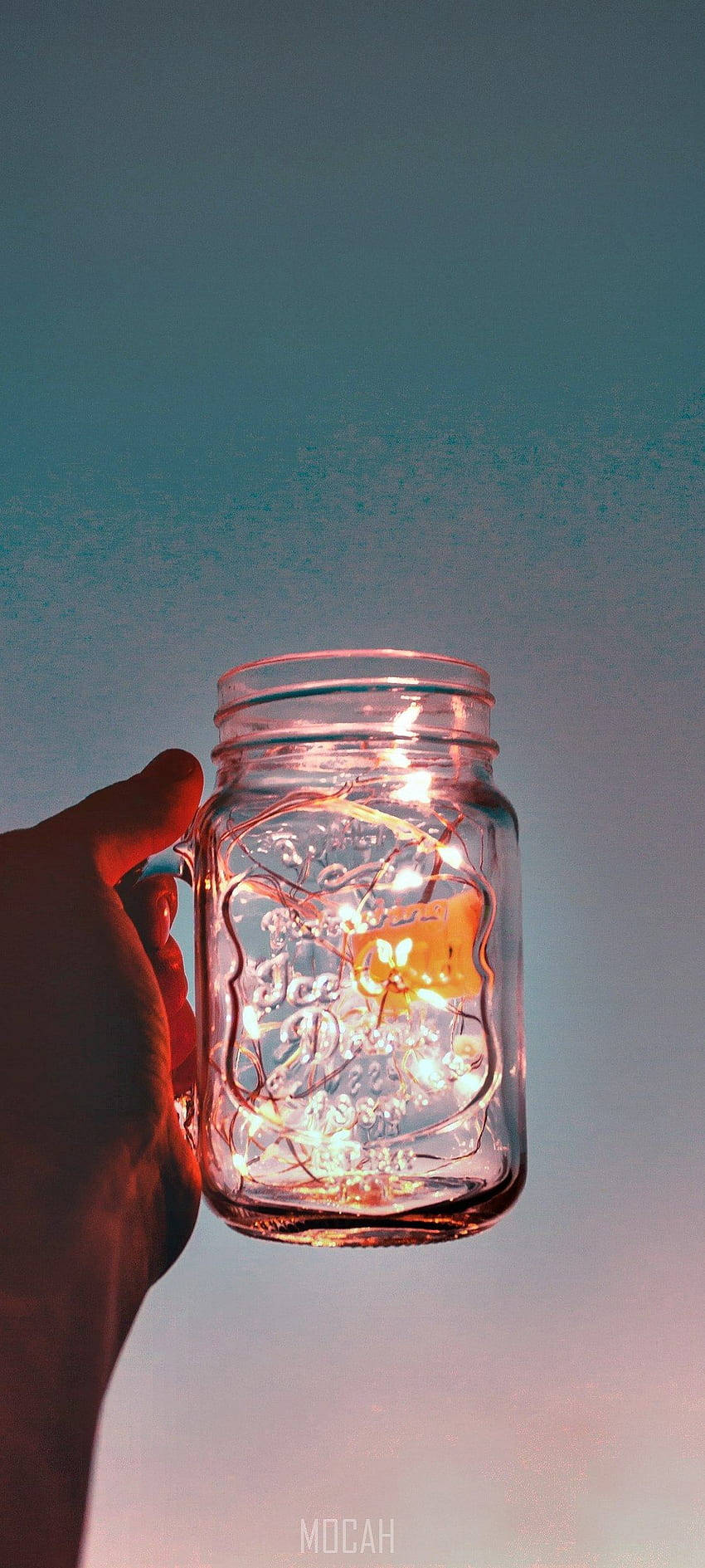 手機 桌布 壁紙 — 一隻手拿著一個裝滿發光仙女燈的玻璃梅森罐，背景是暮色天空。
